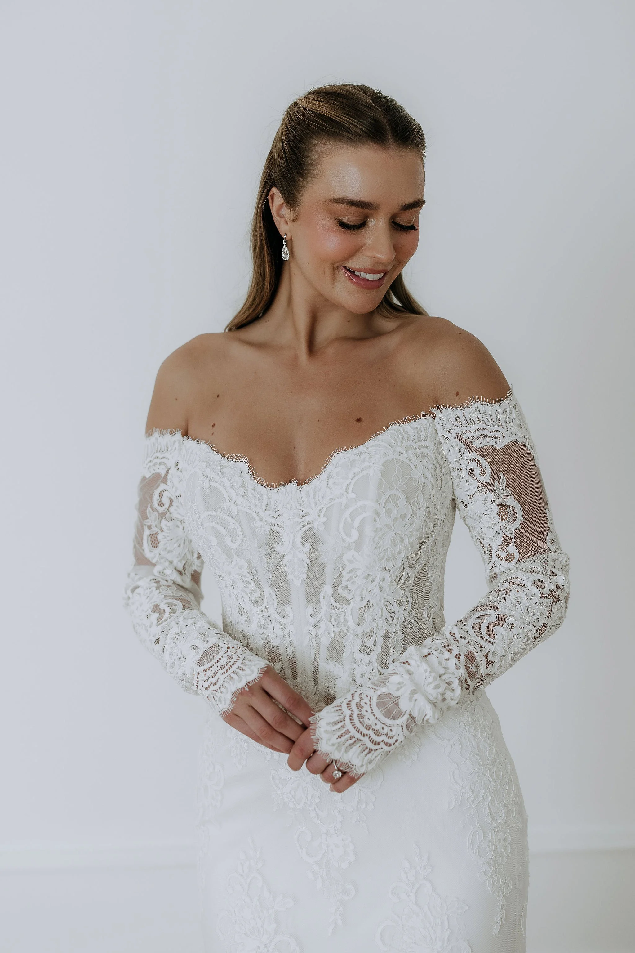 Mimi by Designer Kelly Lin. is a modern fitted lace dress with Bardot neckline and lace sleeves. Make an appointment in Salisbury to try her on.
