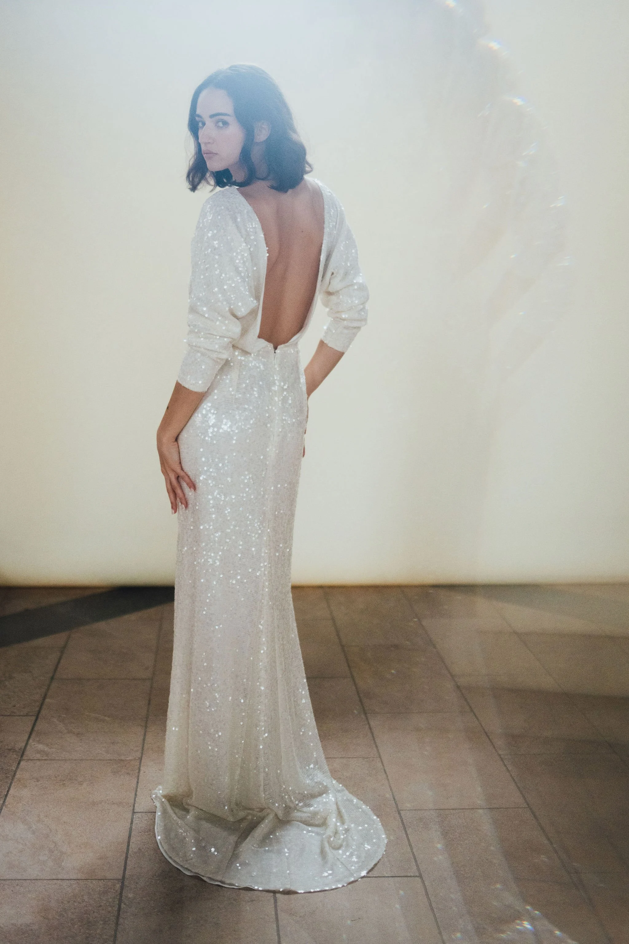 Ophelia Dress by Rolling in Roses – shimmering georgette bridal gown fully embroidered with subtle sequins, featuring a high neckline, plunging open back, fitted skirt with petite godet, and modest train. Includes optional ribbon tie for added securi