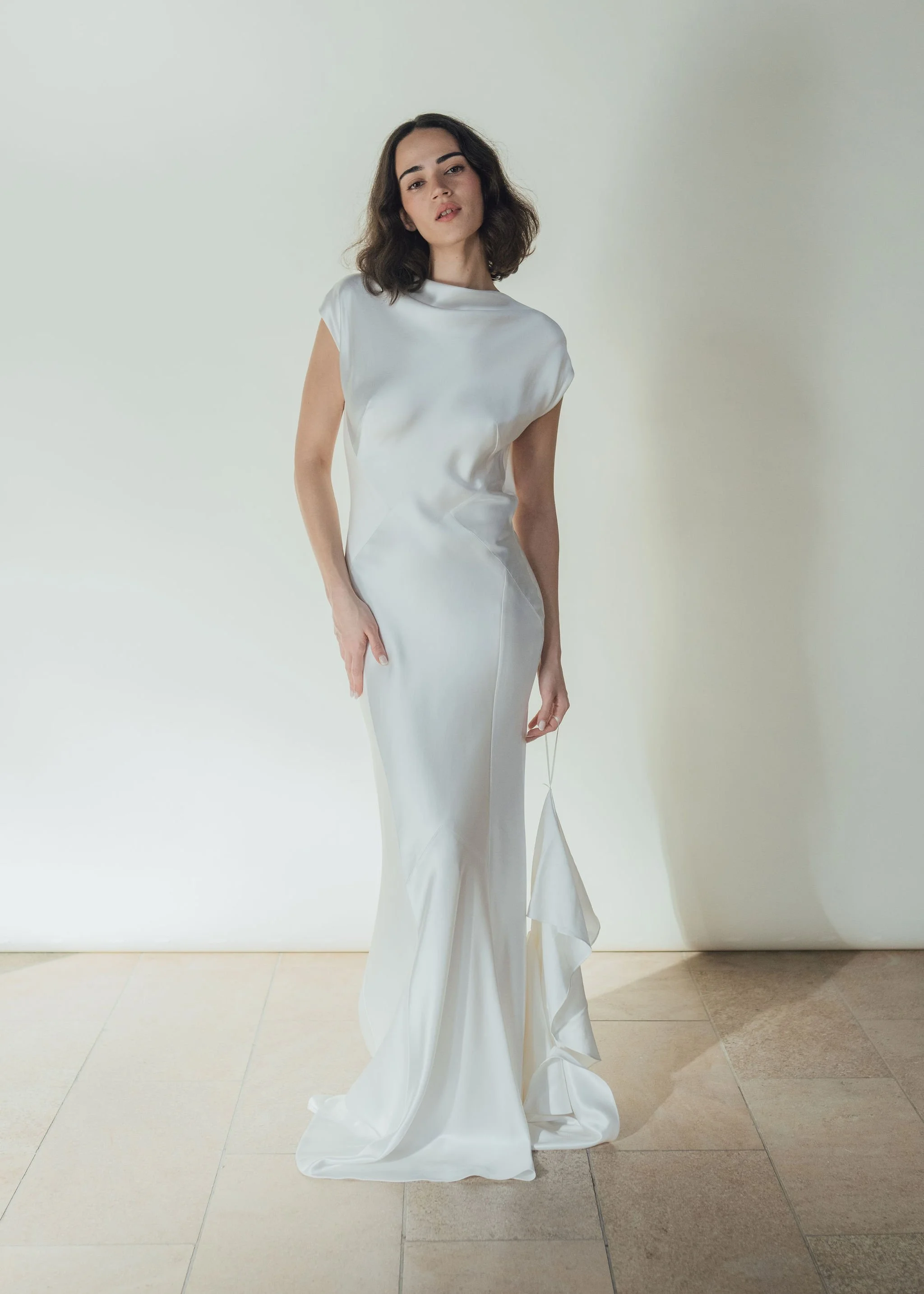 Beatrice Dress by Rolling in Roses – minimalist satin bridal gown with high cowl neckline, open back, angular darts, and detachable wrist loop, crafted from sustainable vegan satin and organic bamboo, available at Lyra Bridal Studio, UK