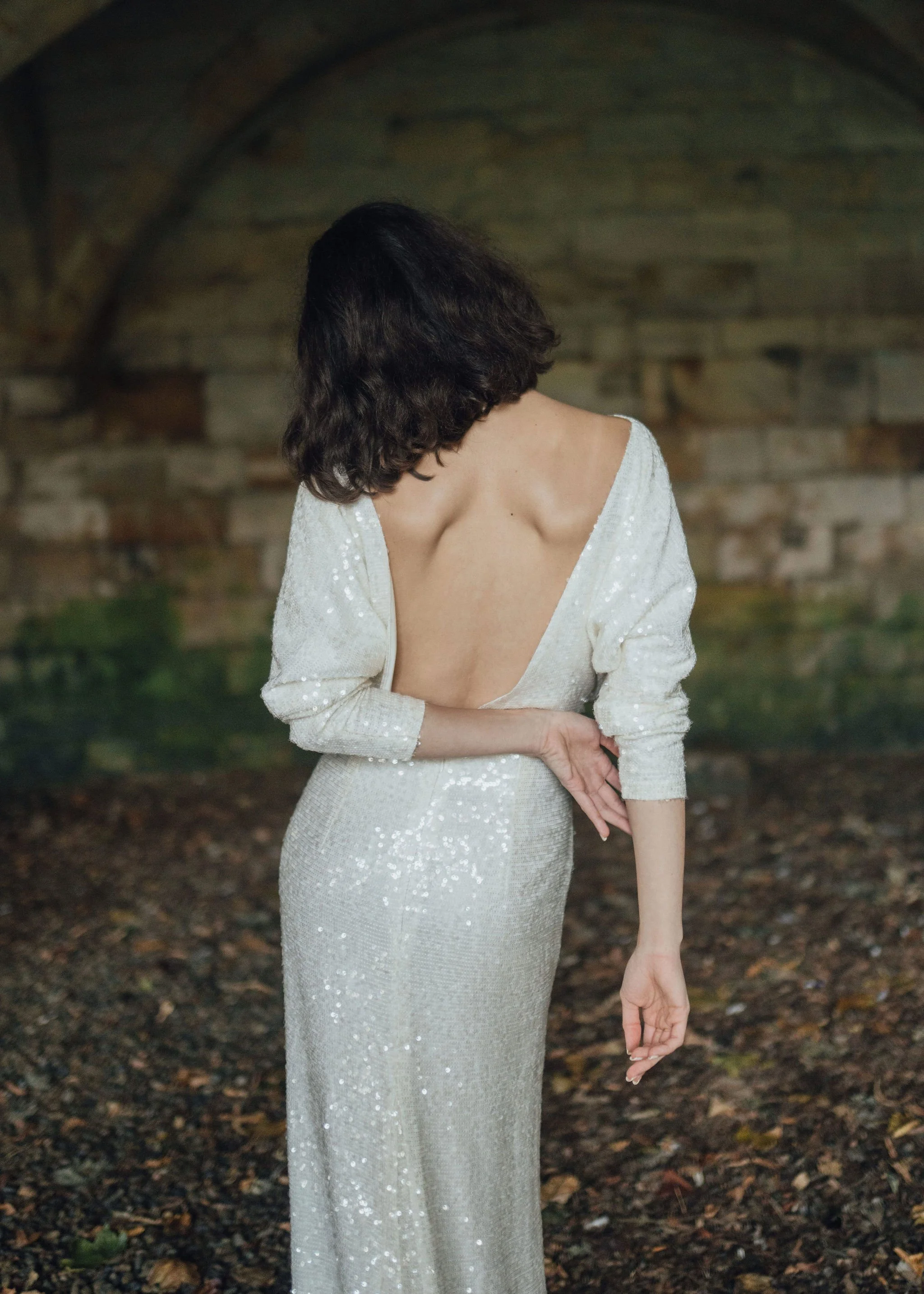 Ophelia Dress by Rolling in Roses – shimmering georgette bridal gown fully embroidered with subtle sequins, featuring a high neckline, plunging open back, fitted skirt with petite godet, and modest train. Includes optional ribbon tie for added securi