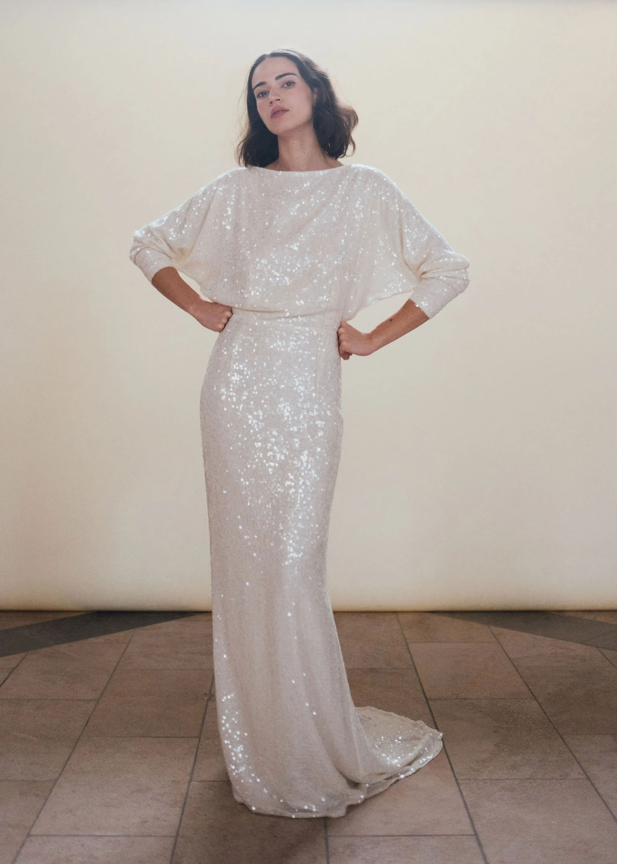 Ophelia Dress by Rolling in Roses – shimmering georgette bridal gown fully embroidered with subtle sequins, featuring a high neckline, plunging open back, fitted skirt with petite godet, and modest train. Includes optional ribbon tie for added securi