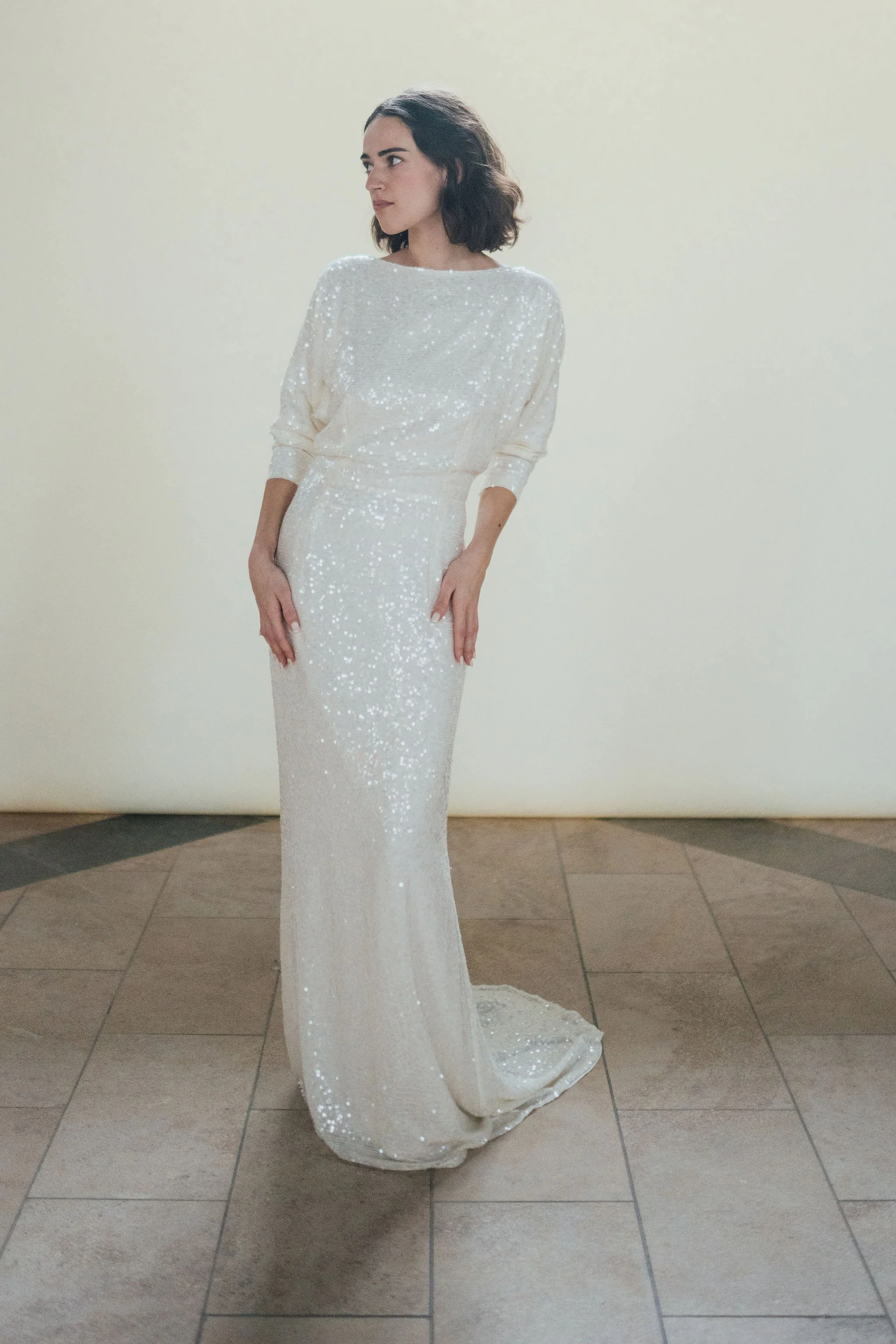 Ophelia Dress by Rolling in Roses – shimmering georgette bridal gown fully embroidered with subtle sequins, featuring a high neckline, plunging open back, fitted skirt with petite godet, and modest train. Includes optional ribbon tie for added securi