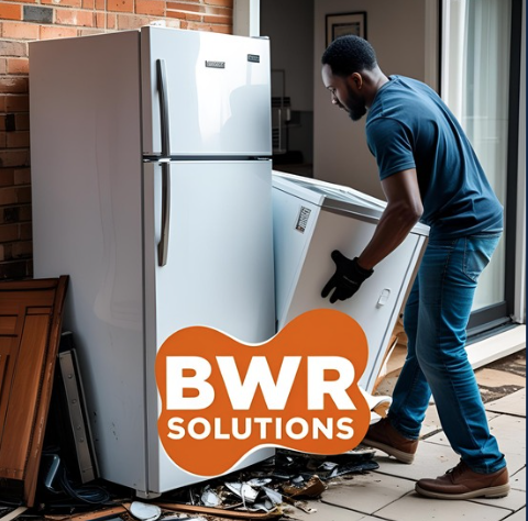A man moving a washing machine outdoors on a porch with a refrigerator nearby.