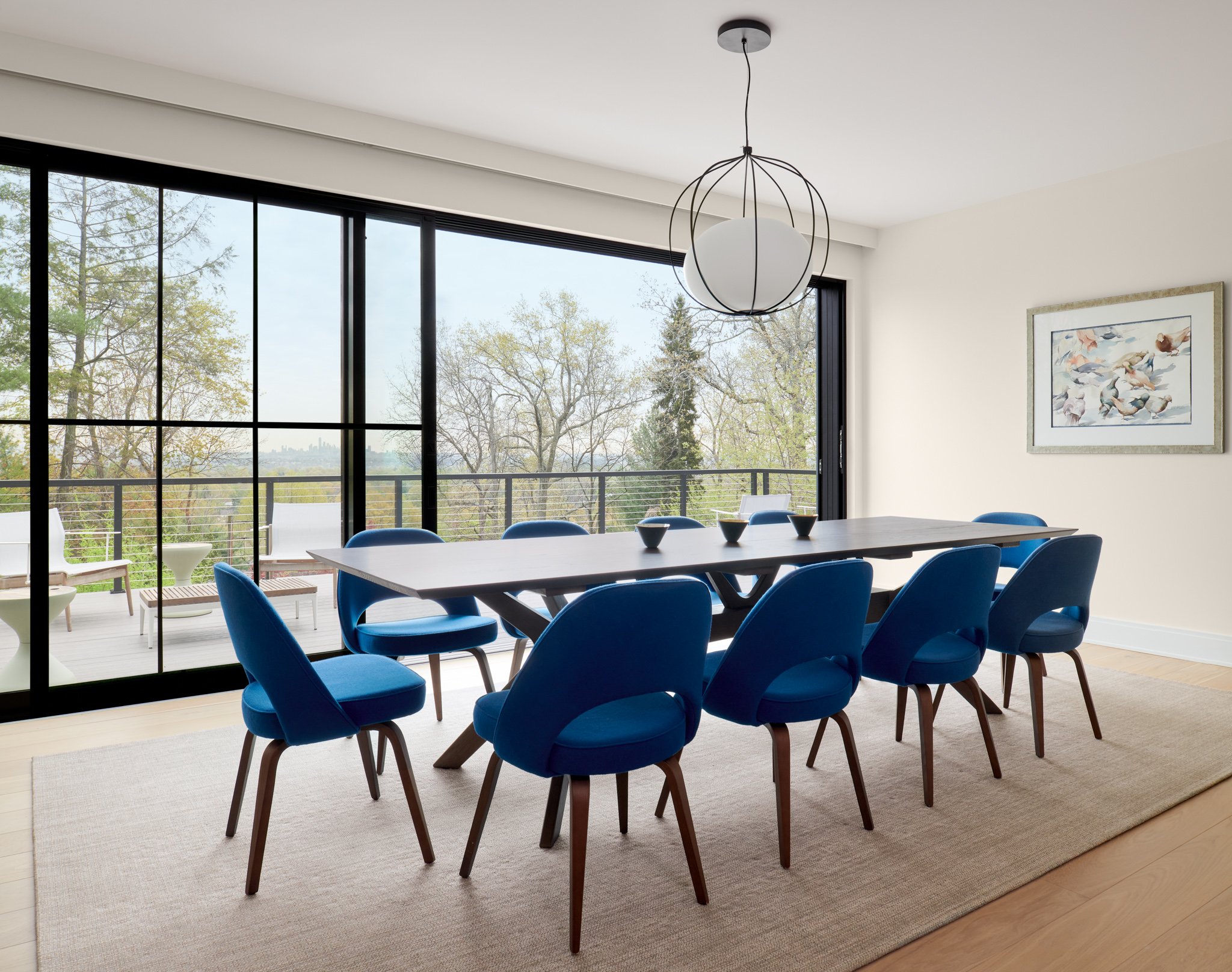 An expansive luxury dining room featuring a custom walnut table, royal blue velvet mid-century chairs, and a sculptural minimalist globe pendant light.