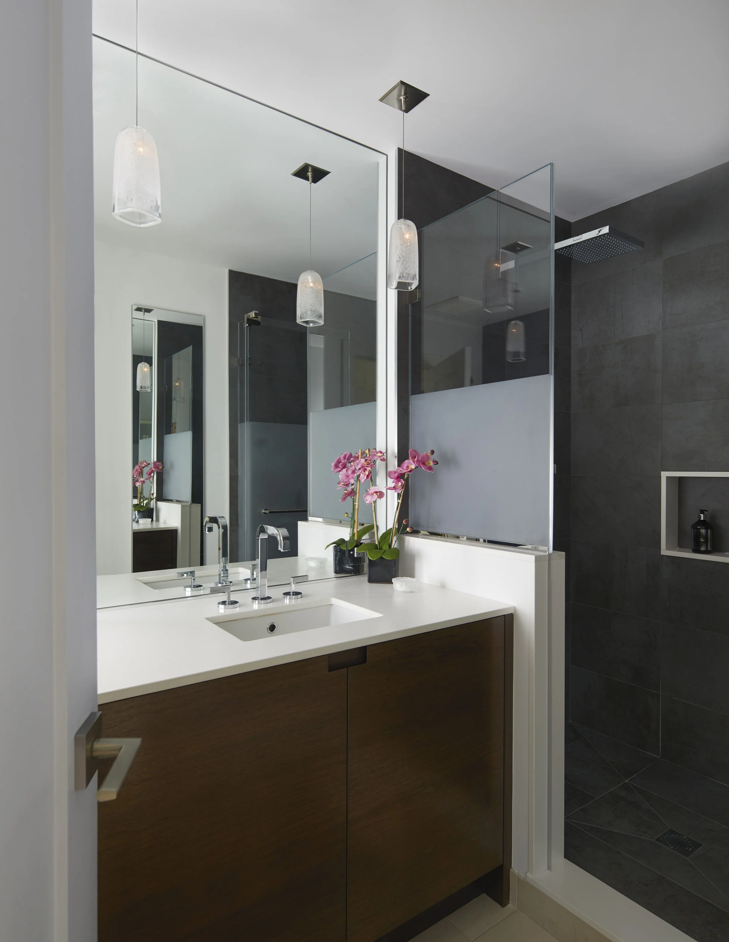 High-end bathroom renovation featuring a custom walnut floating vanity, dark graphite tile, and architectural pendant lighting by a luxury interior architect