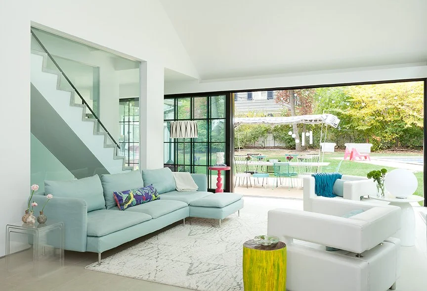 Open-plan living room in contemporary addition to traditional English stucco home with floating glass staircase, floor-to-ceiling steel sliding doors, and lush garden views — New Jersey luxury renovation