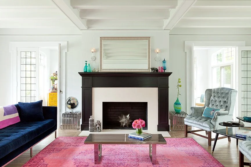Renovated living room in traditional English stucco home preserving original coffered ceiling with bold eclectic interior design, black painted fireplace surround, and navy velvet sofa — NJ