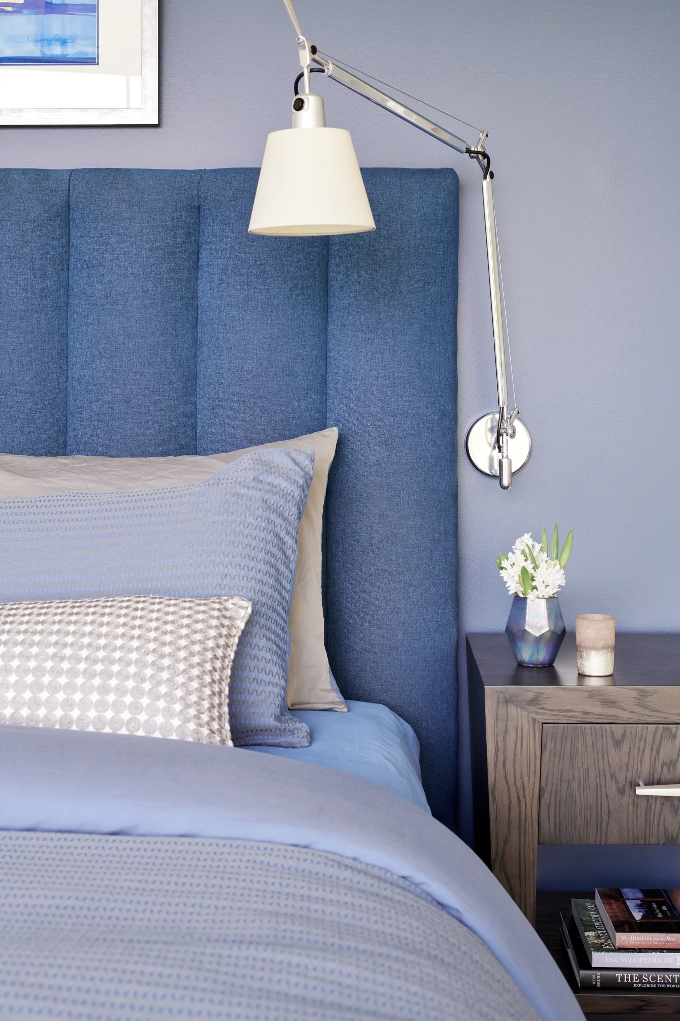 Primary bedroom retreat featuring a custom channel-tufted blue denim fabric headboard, periwinkle walls, an articulating chrome wall sconce, and a dark oak nightstand.