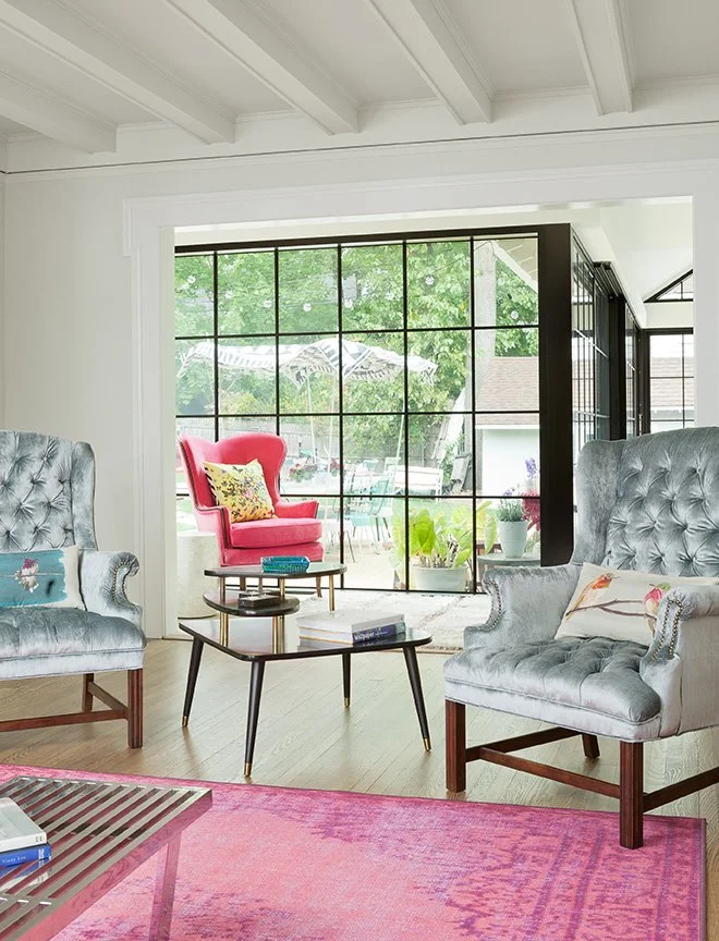 Luxury sitting room renovation in traditional English stucco home with tufted velvet wingback chairs, bold pink accent chair, and steel-frame window wall opening to garden — Montclair NJ