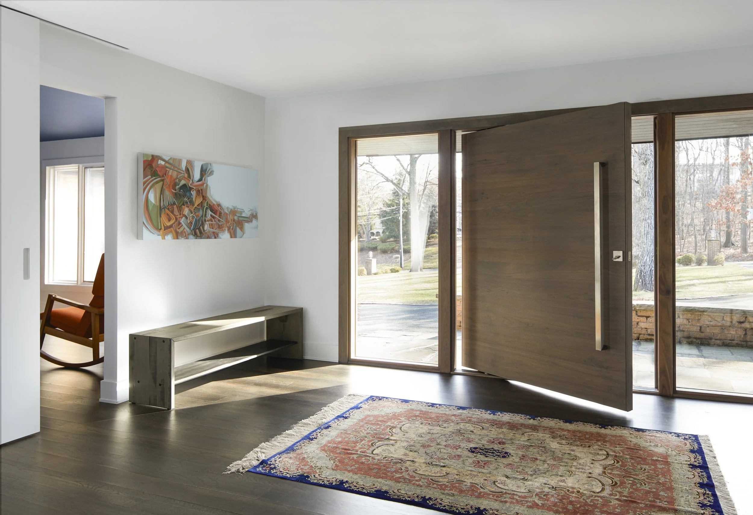 Contemporary grand foyer entry with a luxury oversized walnut pivot door, oak flooring, and editorial staging for a high-end modern renovation.