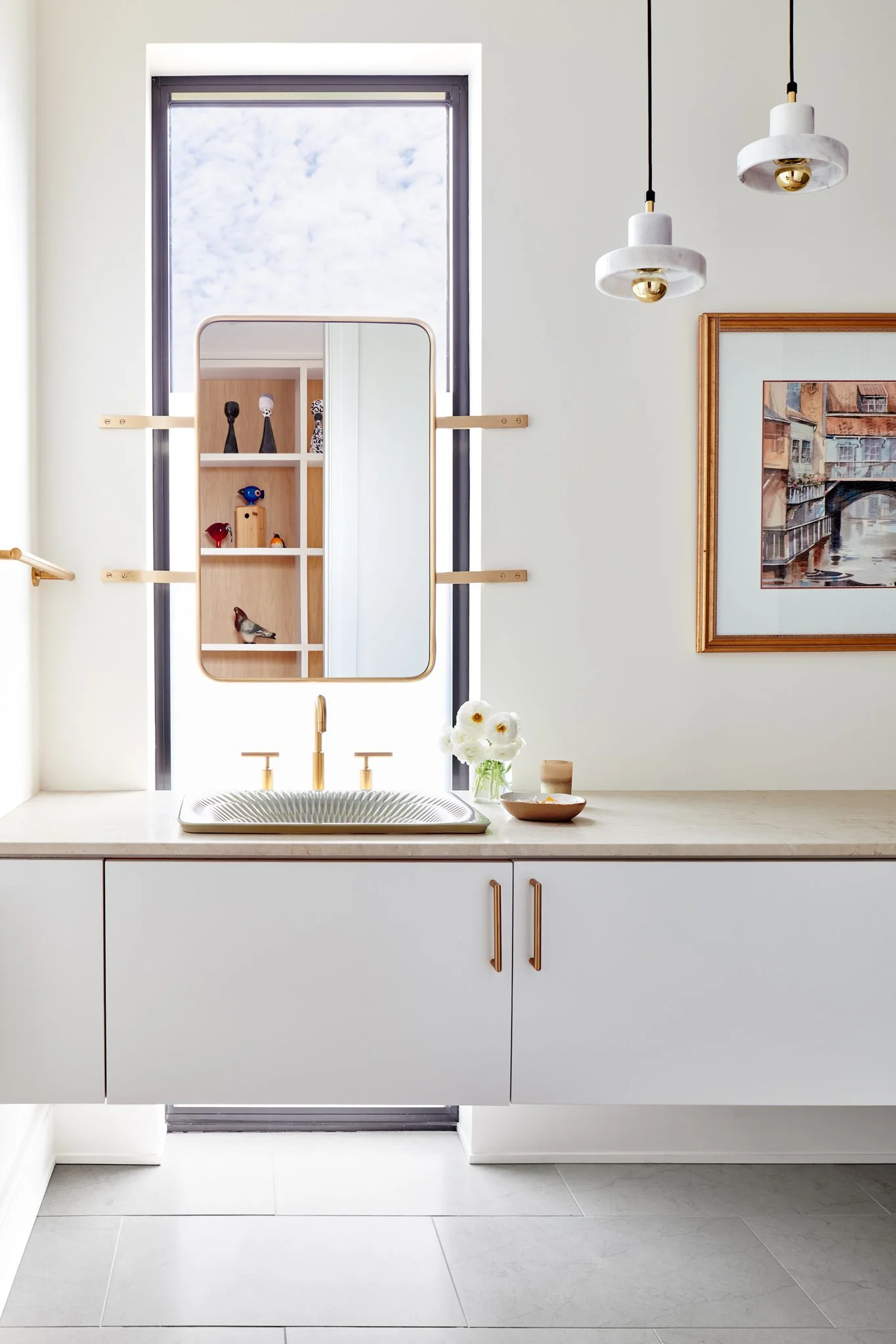 Architectural powder room with a custom floating white vanity, a limestone countertop, an asymmetrical textured sink basin, and a mirror suspended over a tall window slot.