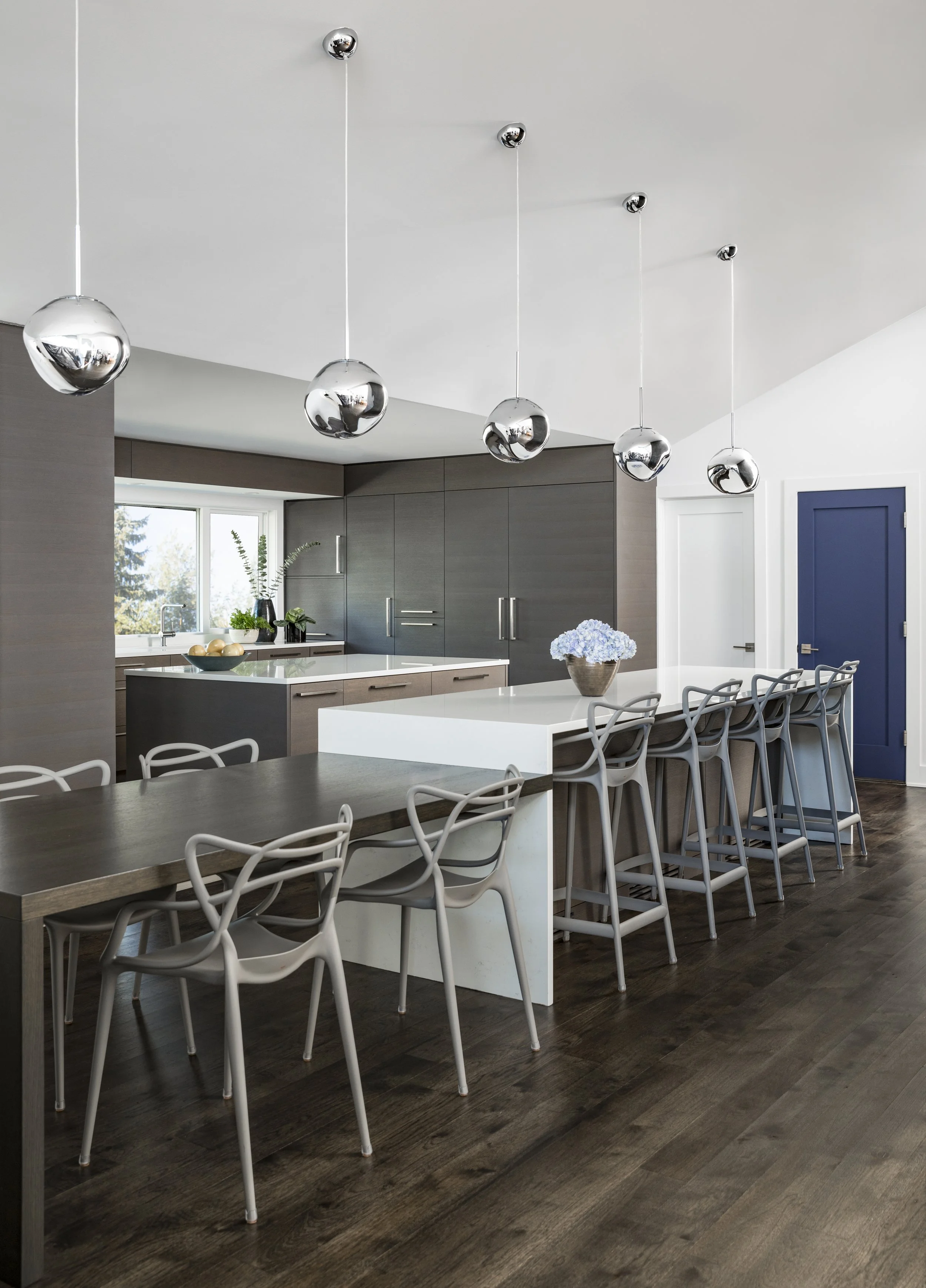 Vertical view of a luxury contemporary kitchen renovation with minimalist dark wood cabinetry, integrated appliances, and a crisp white quartz countertop.