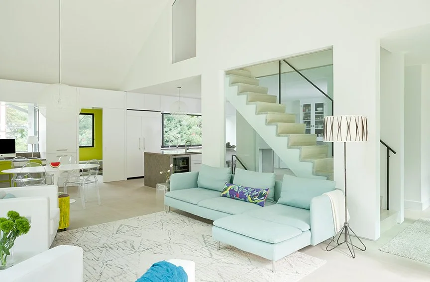 Bright open-plan great room renovation in English stucco home modern addition connecting living, kitchen, and dining with floating glass staircase and soaring vaulted ceiling — Montclair NJ