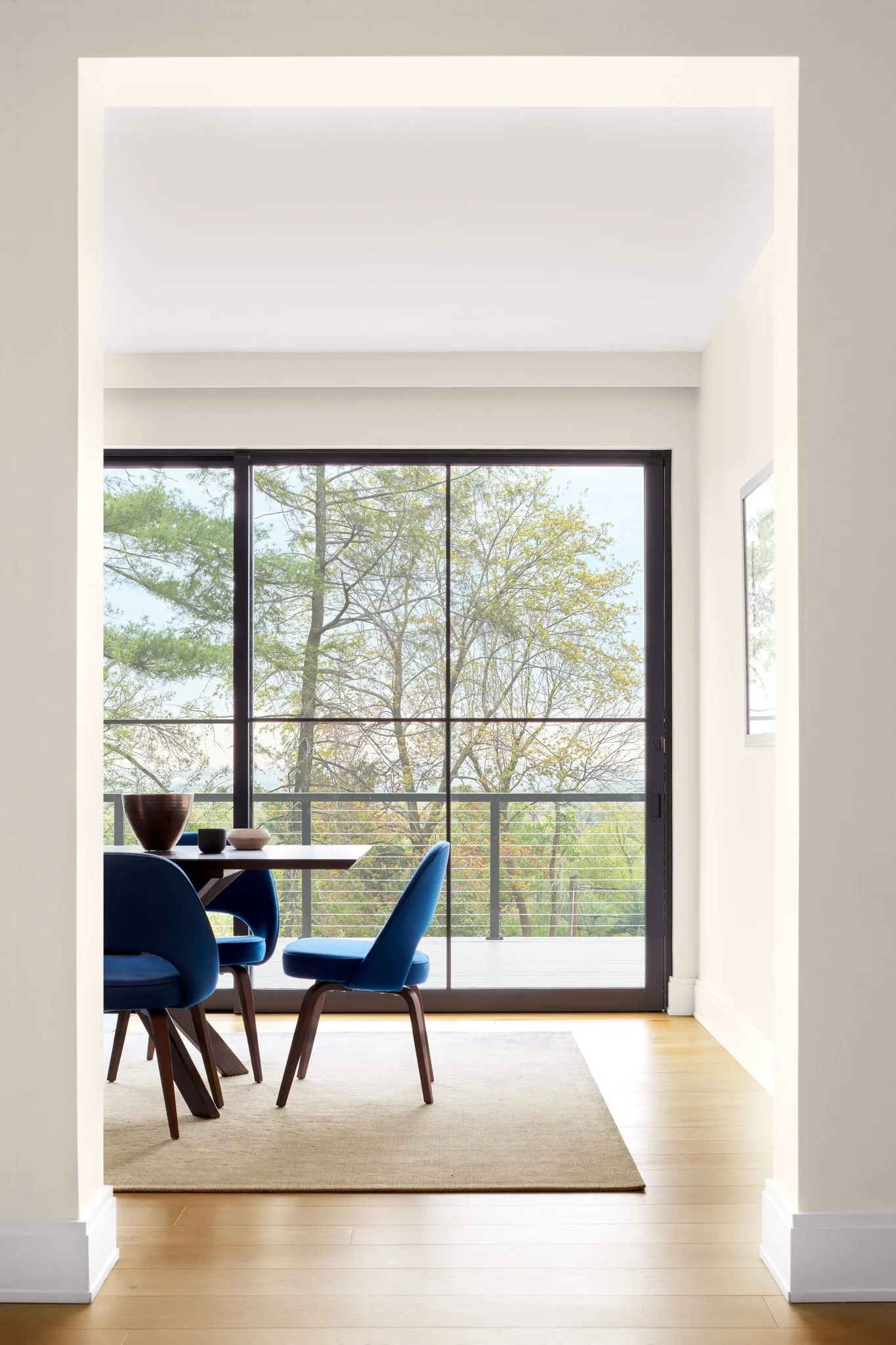 Luxury dining room layout looking through floor-to-ceiling black frame sliding glass doors to a large outdoor entertaining deck and mature treetops
