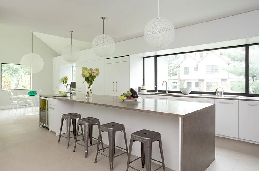 Luxury all-white kitchen renovation in English stucco home contemporary addition with large concrete topped island, industrial metal barstools, woven globe pendants, and full-width steel frame windows — New Jerse