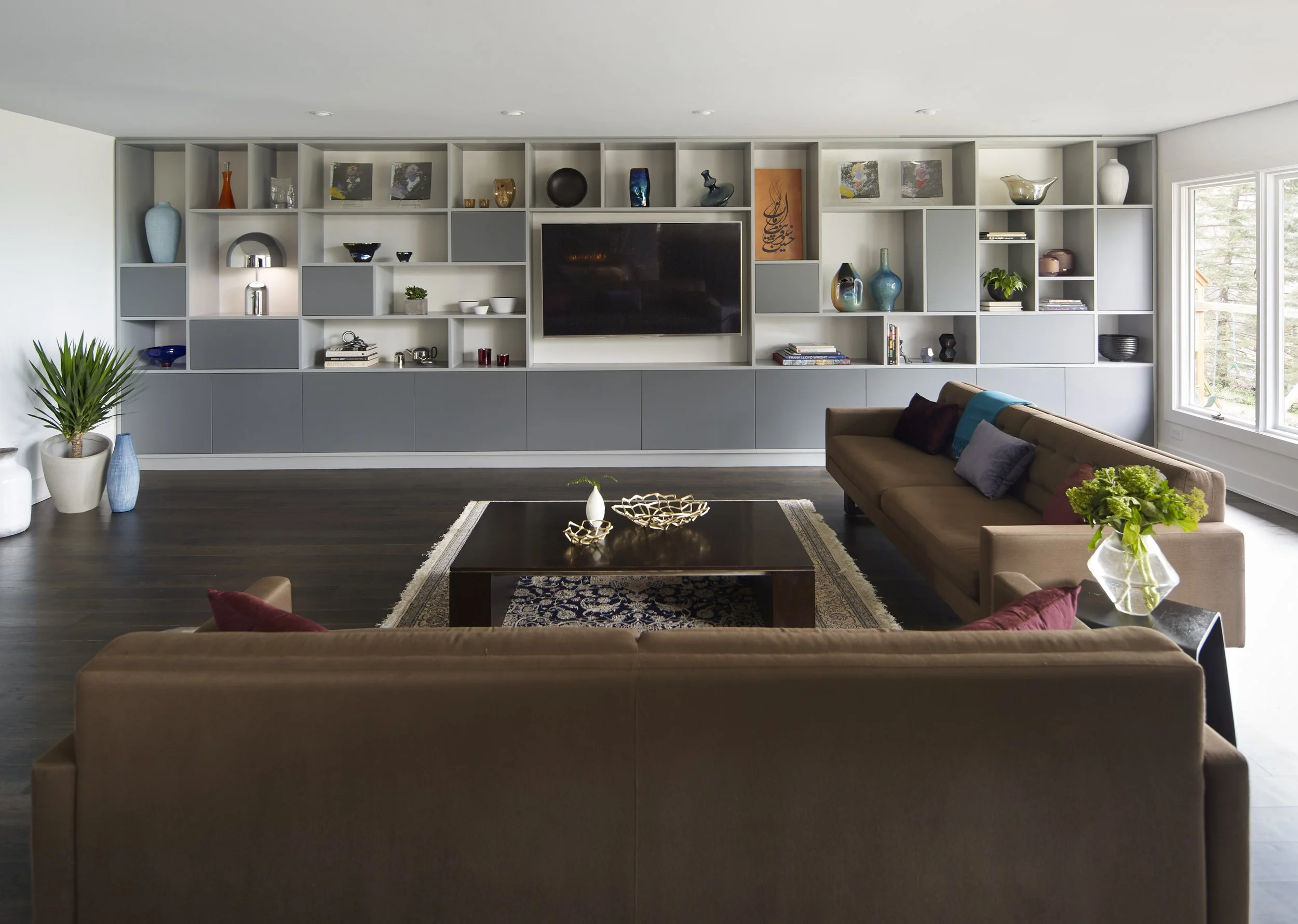 Symmetrical, high-end living room renovation with a wall-to-wall custom media console and display shelving, dark hardwood floors, and minimalist editorial furniture styling.