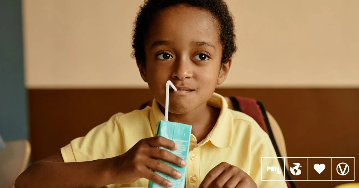A young boy with curly hair in a yellow polo shirt drinking from a juice box with a straw.