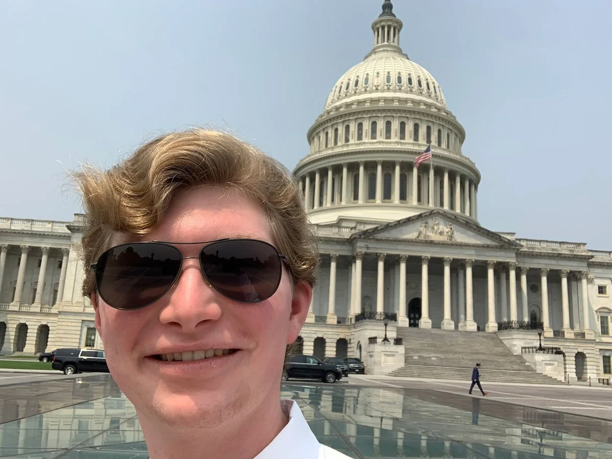 Young man wearing sunglasses smiling in front of the U.S. Capitol building in Washington, D.C.