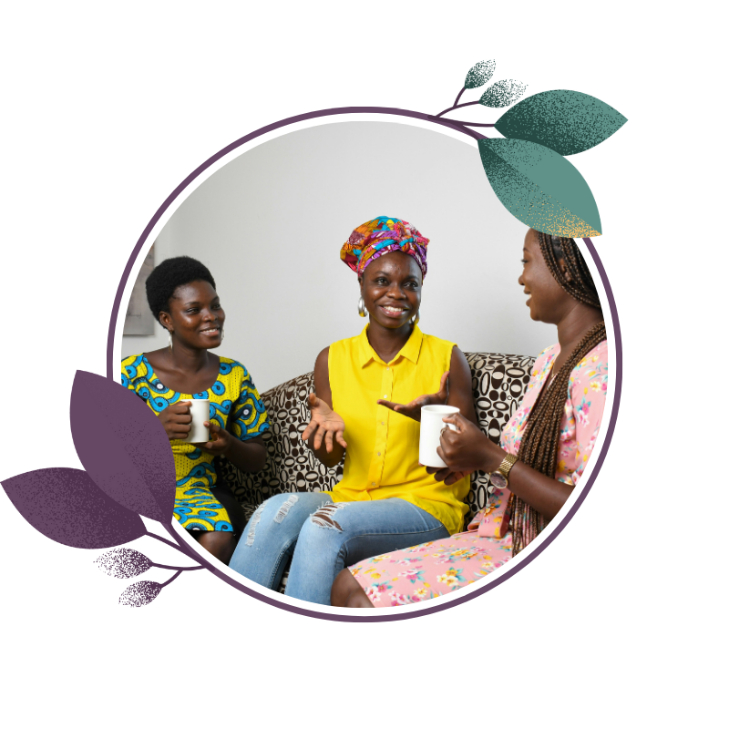 Three women sitting on a couch, smiling and talking, each holding a white mug, with a gray and patterned cushion behind them.