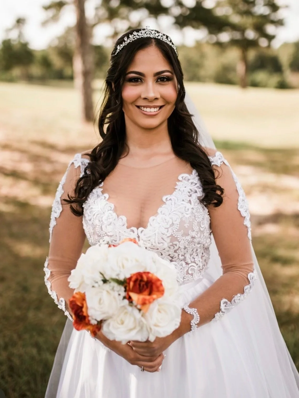A smiling bride with long dark hair in a white wedding dress holding a bouquet of white and orange flowers outdoors. HS Glam Makeup Bridal Portfolio