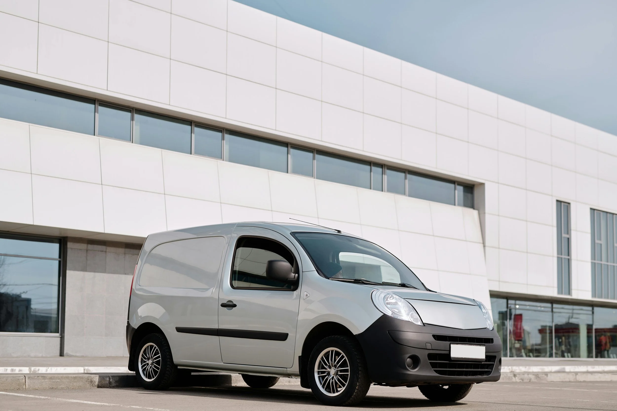 Silver compact cargo van parked outside modern building with white facade and large windows