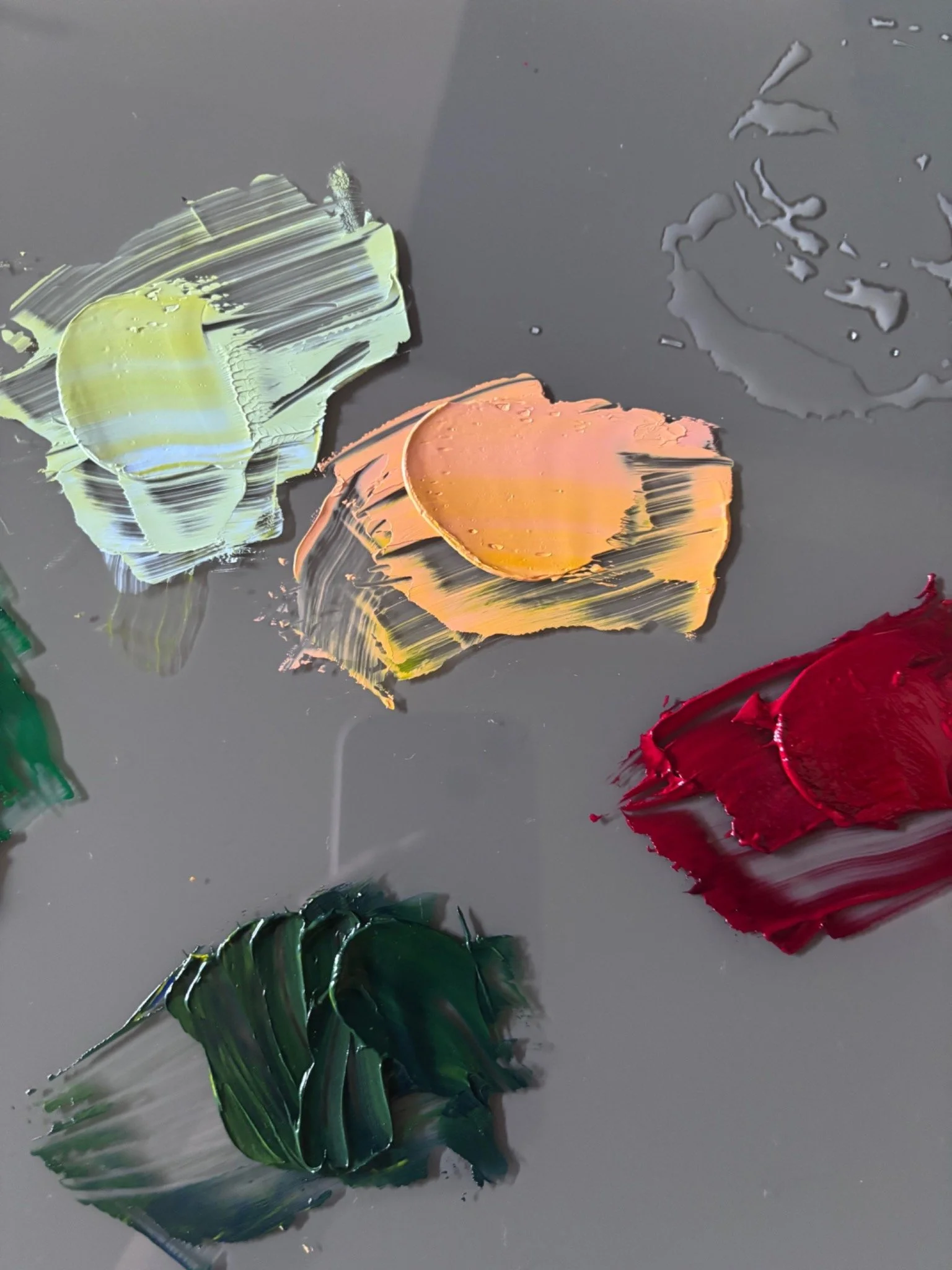 Soft green, peach, burgundy, and deep green paint mixed on a gray palette.