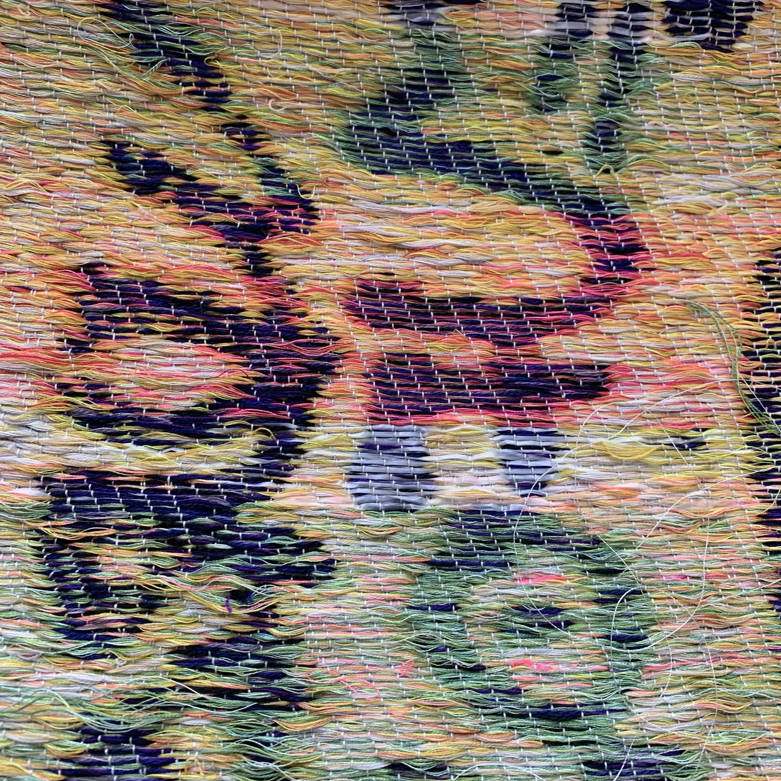 Close-up of a woven textile with multicolored threads including yellow, pink, blue, and green.
