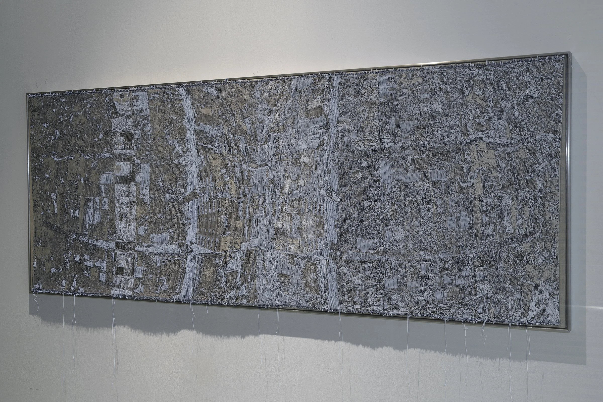 Mixed media artwork with abstract patterns in black, white, and gray colors, mounted on a gray wall.