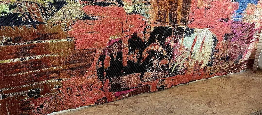 A colorful tapestry with a pixelated image of two children playing, with warm tones of pink, orange, and red, hanging on a wall.