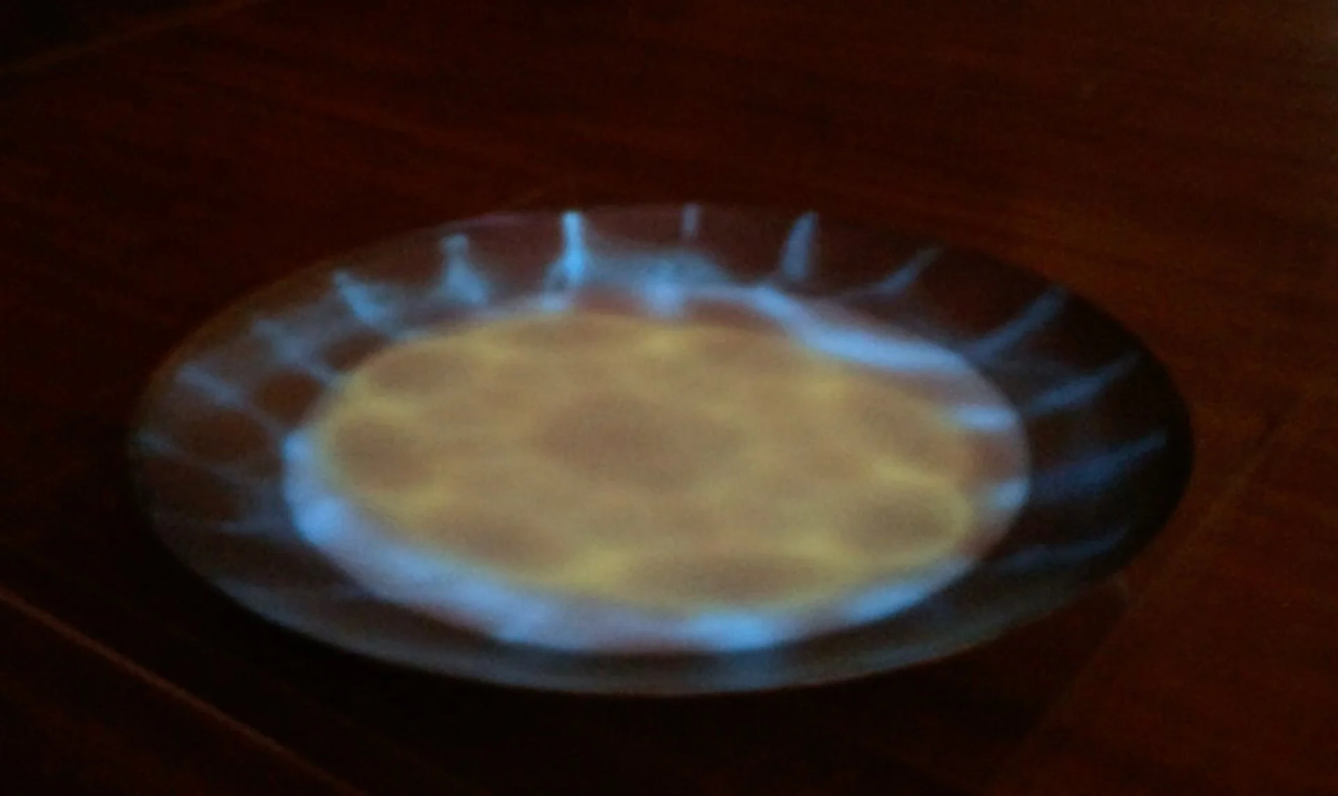 A close-up of a small, round, metallic object with a glowing blue ring around its edge, situated on a wooden surface.
