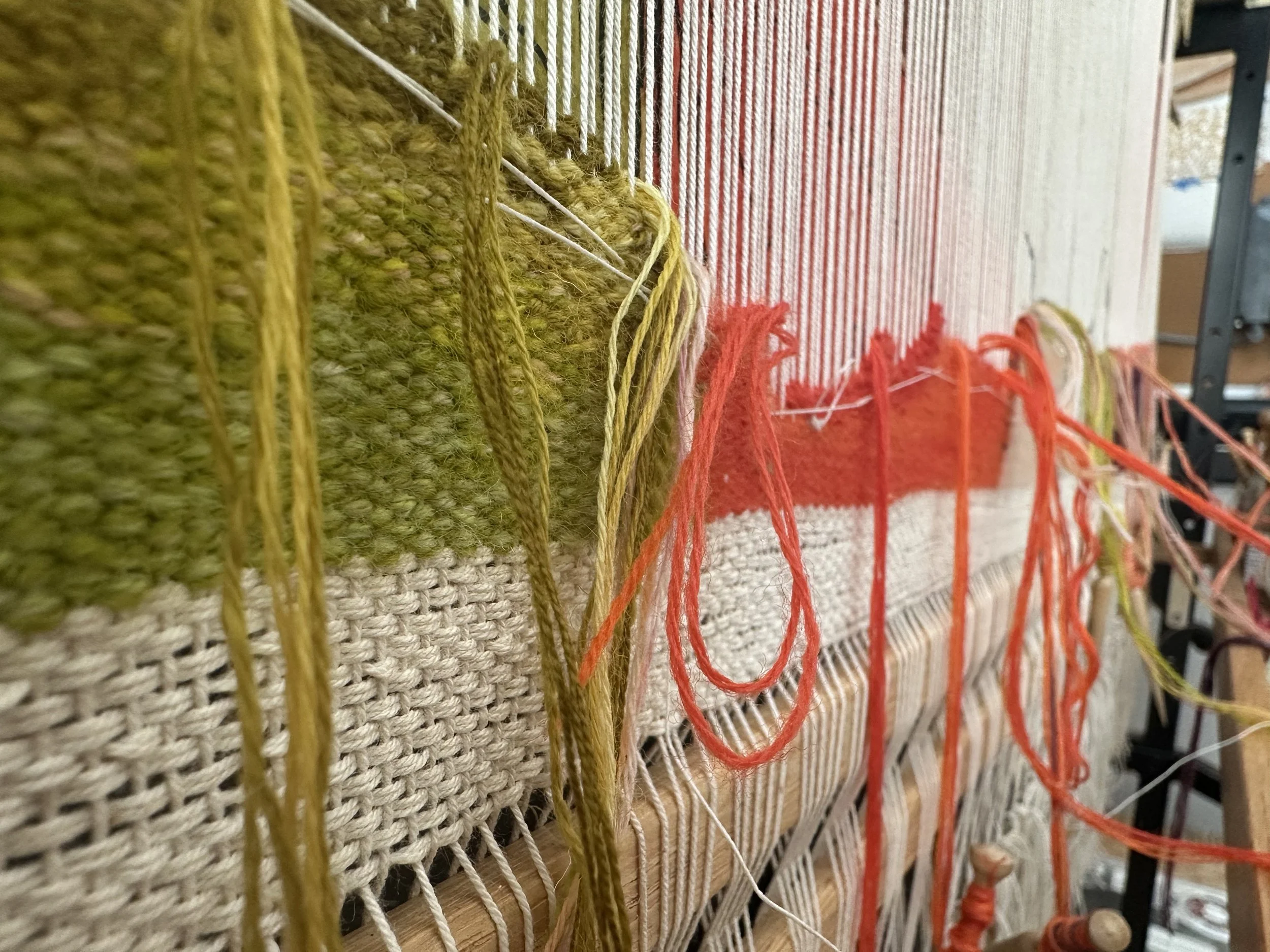 Close-up view of a textile art piece with different colored yarns, including yellow, red, and green, woven into a patterned fabric.