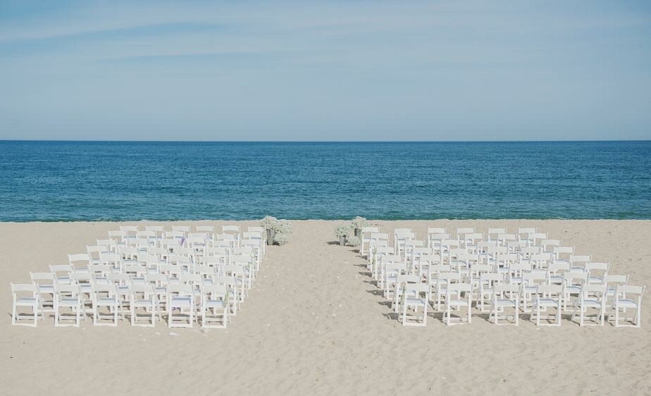 A beach wedding setup with rows of white chairs facing the ocean