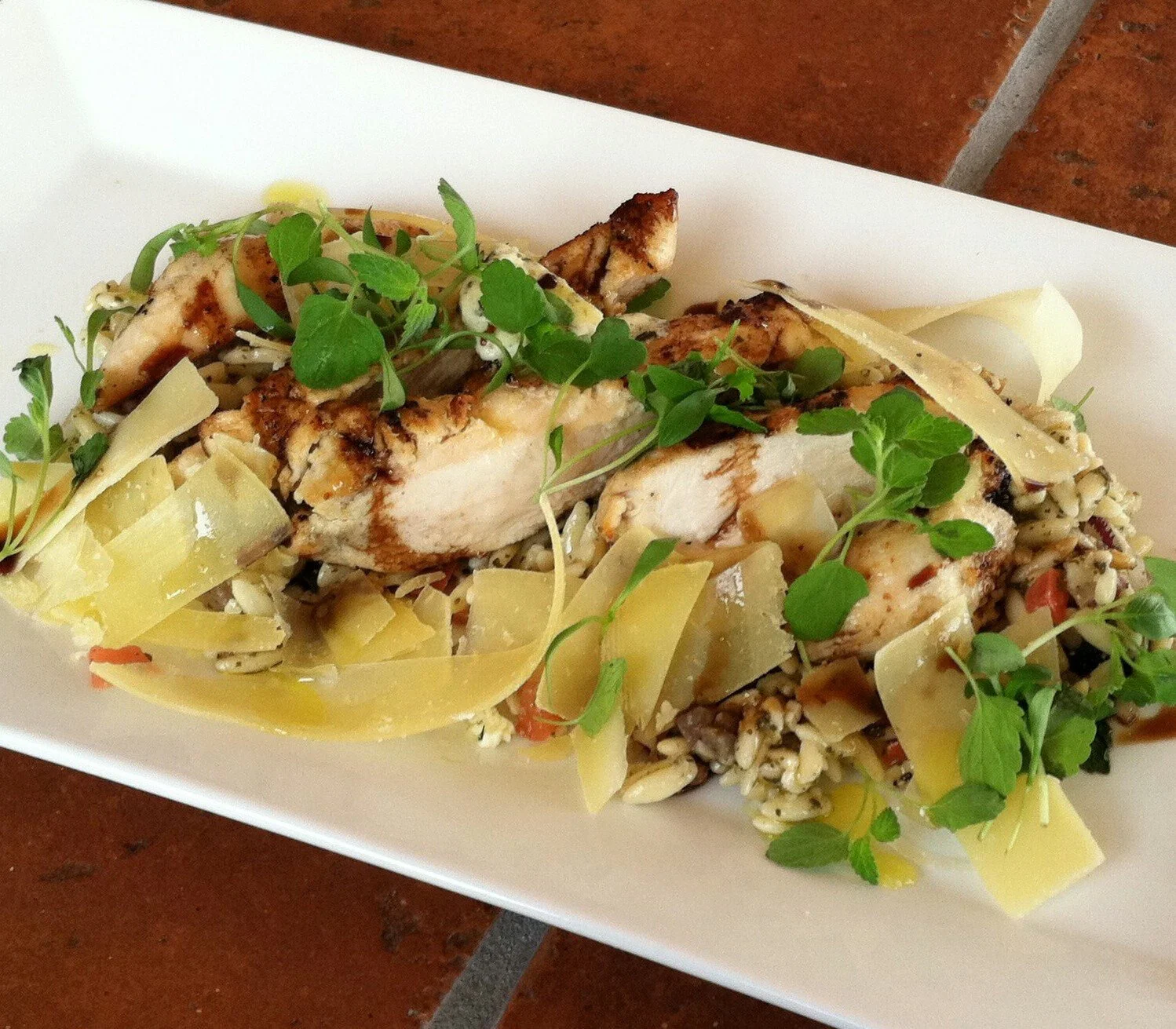 A grilled chicken salad with shaved cheese and greens