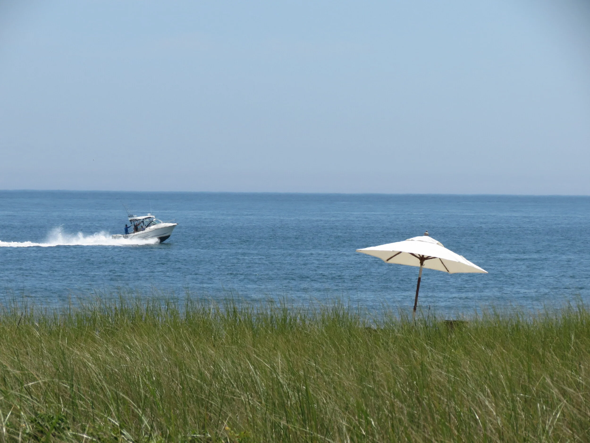 A beach scene featuring a Catania umbrella on grassy land and a boat on the water