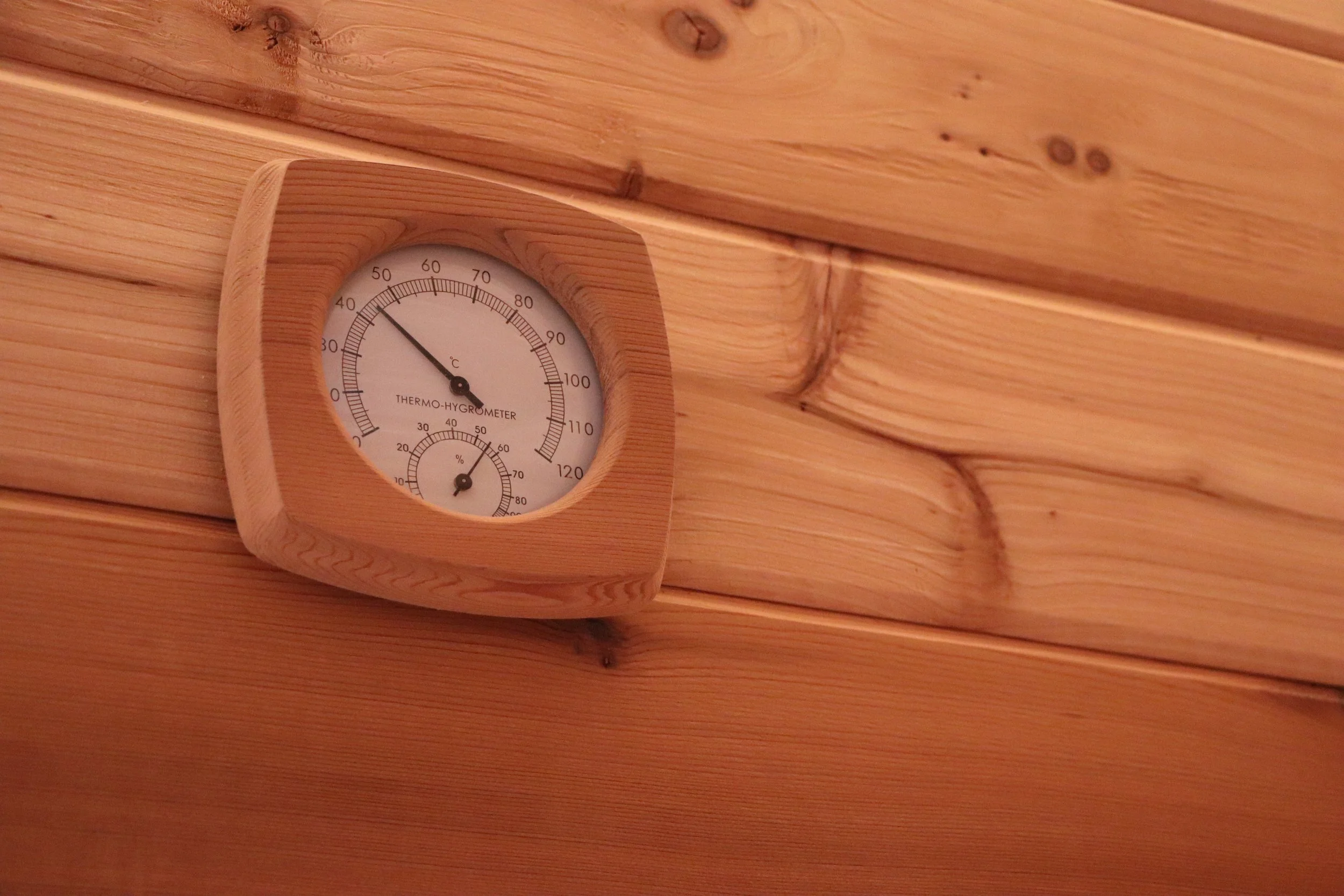 A wooden-framed thermometer and hygrometer mounted on a wooden wall.