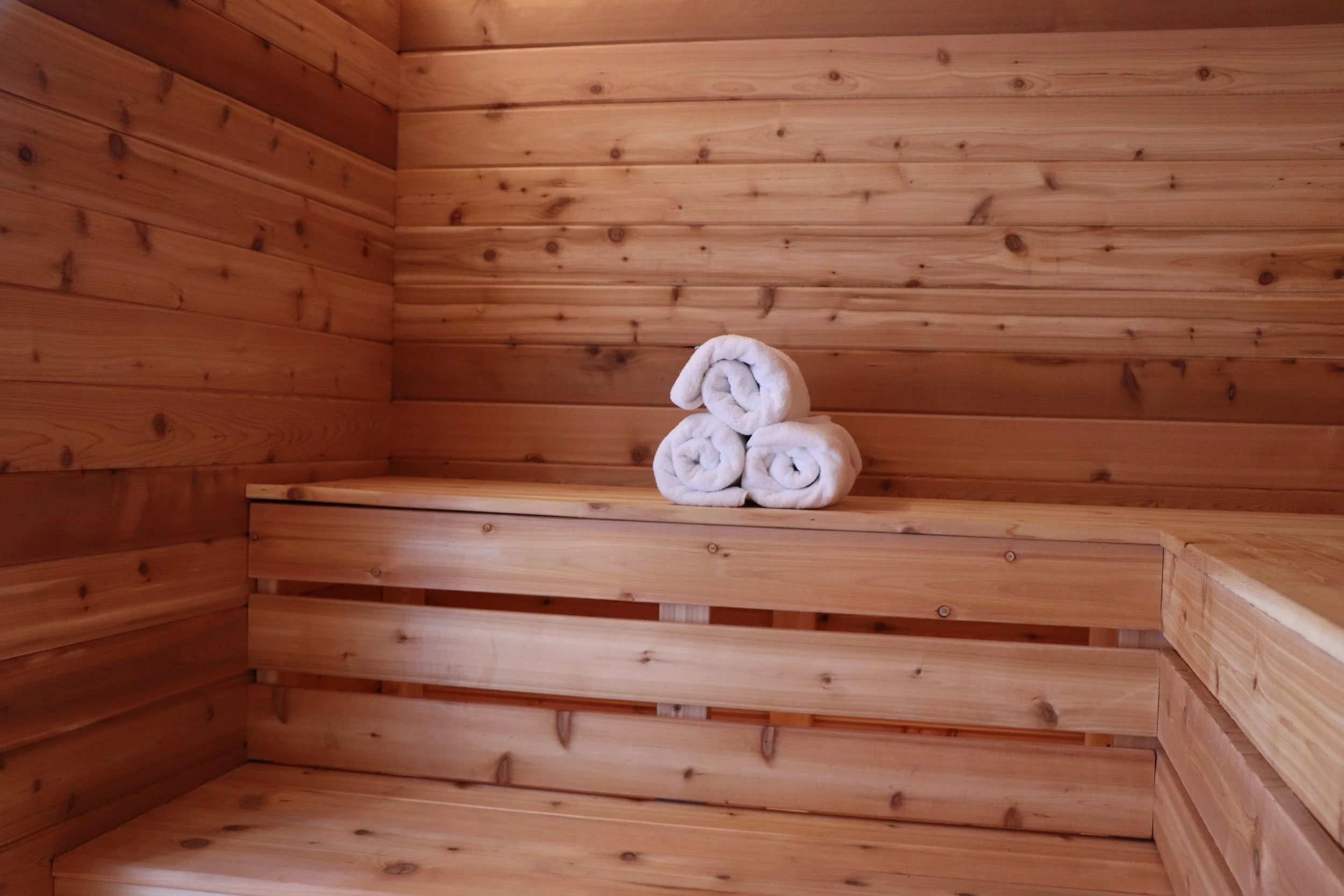 Inside a wooden sauna with three rolled white towels placed on a bench.
