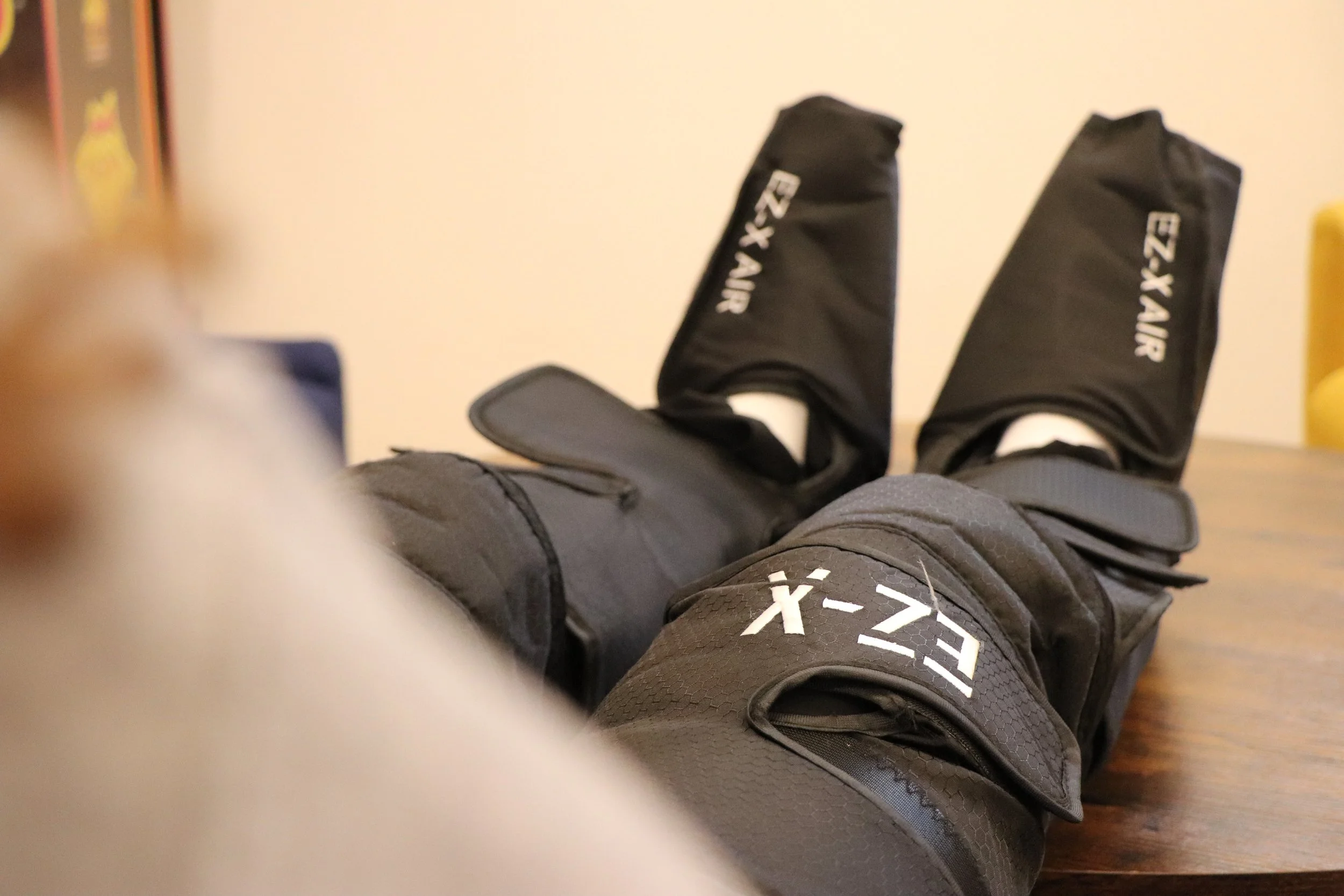 Close-up of a person wearing black X-TX AIR sports shoes and gray athletic pants, lying on a wooden floor indoors.