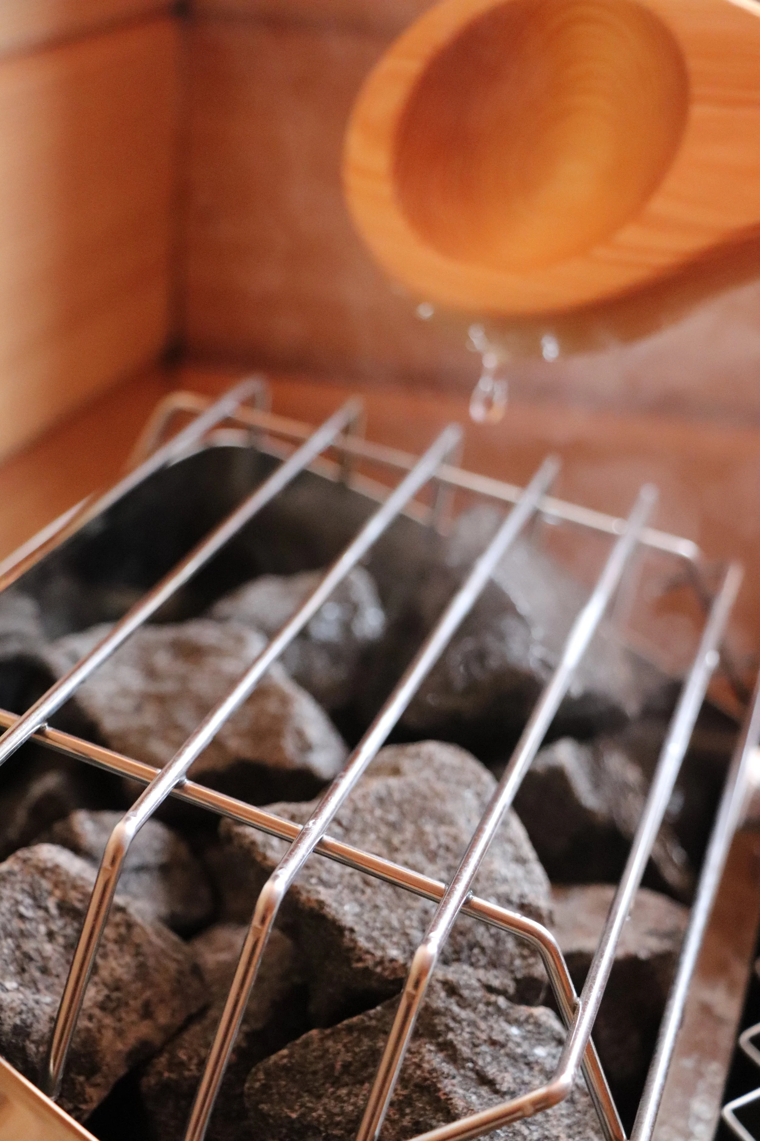 Close-up of a metal rack with rocks underneath, a wooden bowl hanging above, and water droplets falling from the bowl.