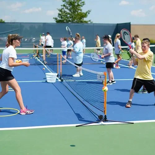 Group of children and teenagers playing pickleball on a blue outdoor court under a clear sky.