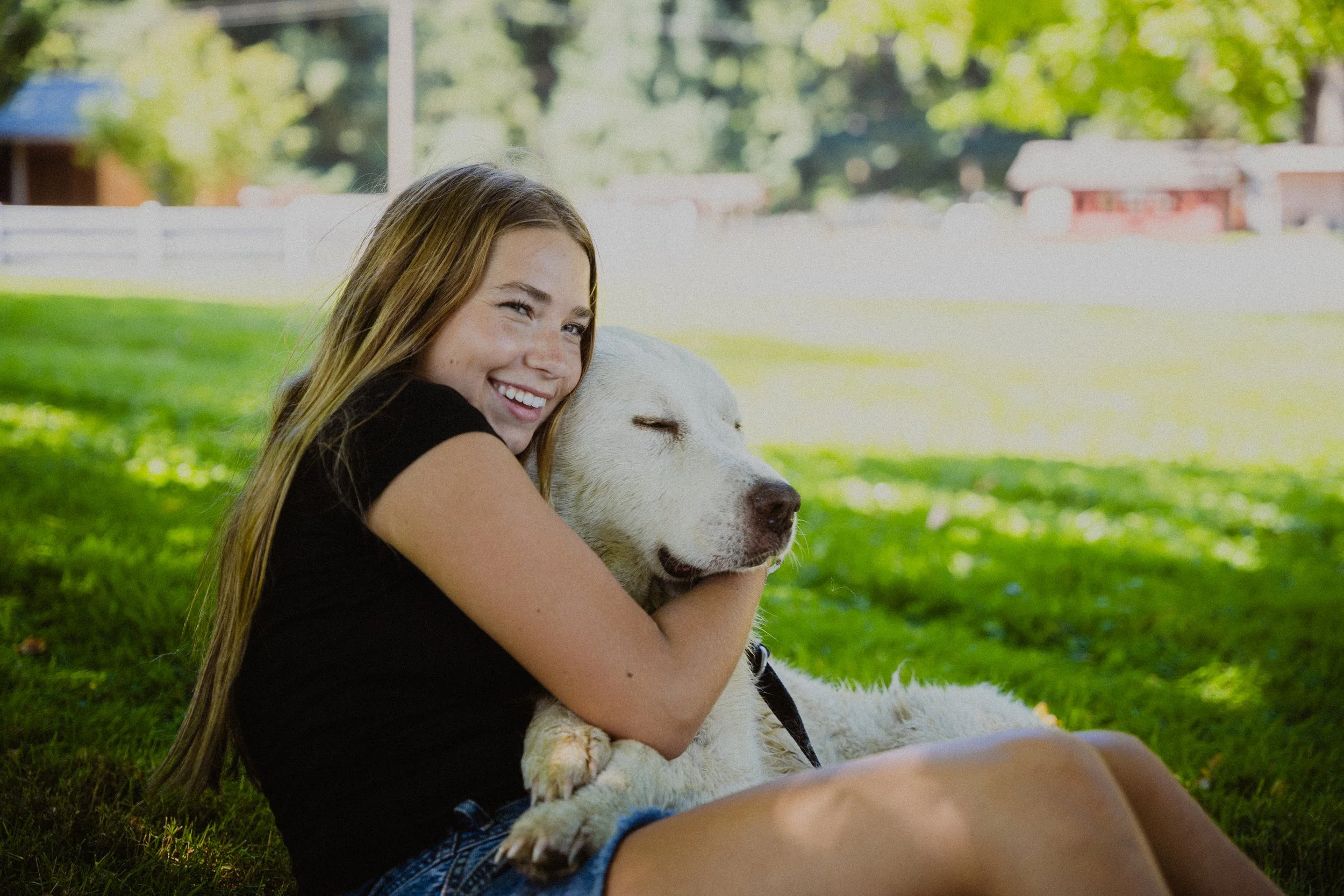 Hartley Wilcox sitting in the grass outdoors with a farm dog at Wilcox Farms.