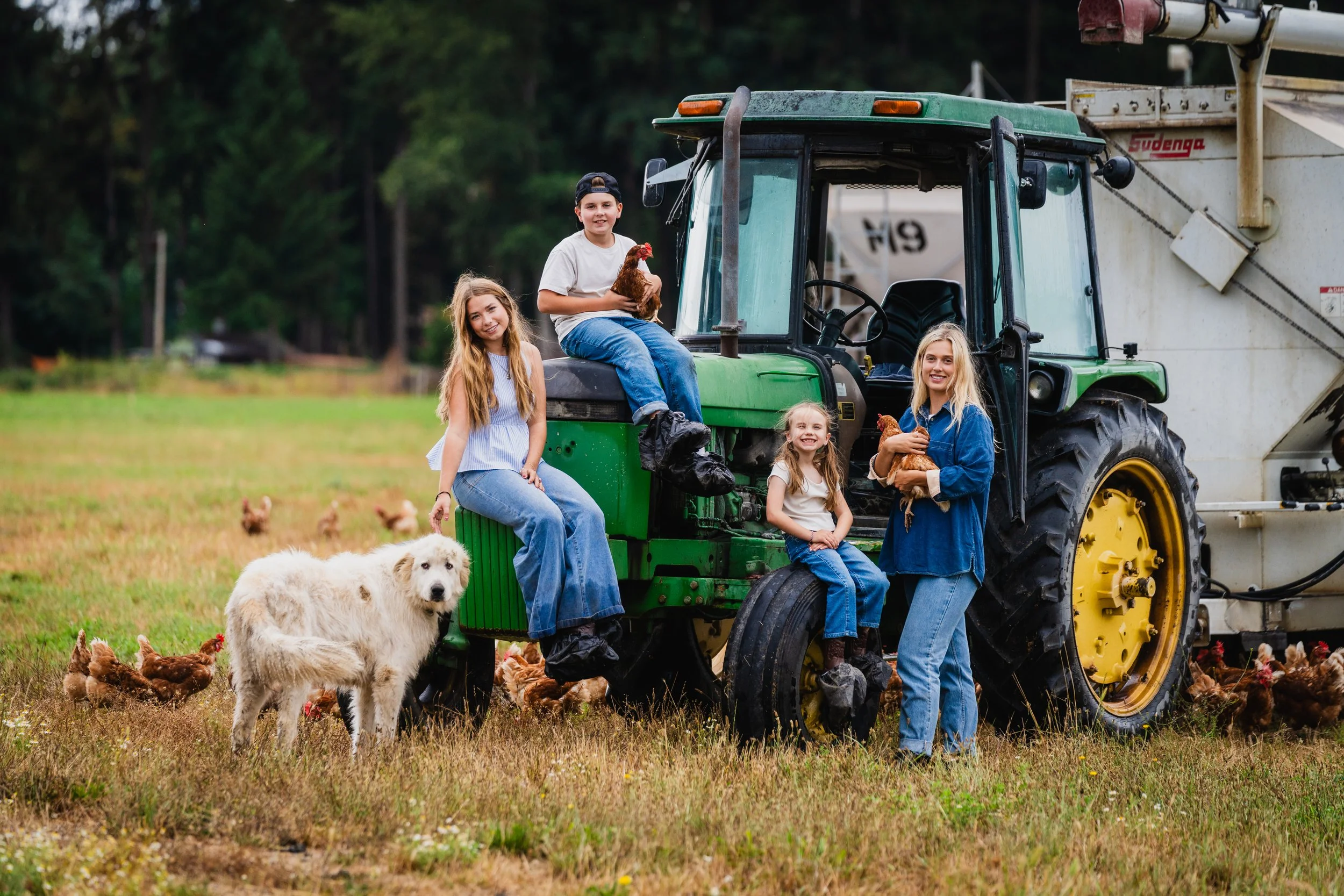 Group of five children and a dog on a farm with chickens and a tractor.