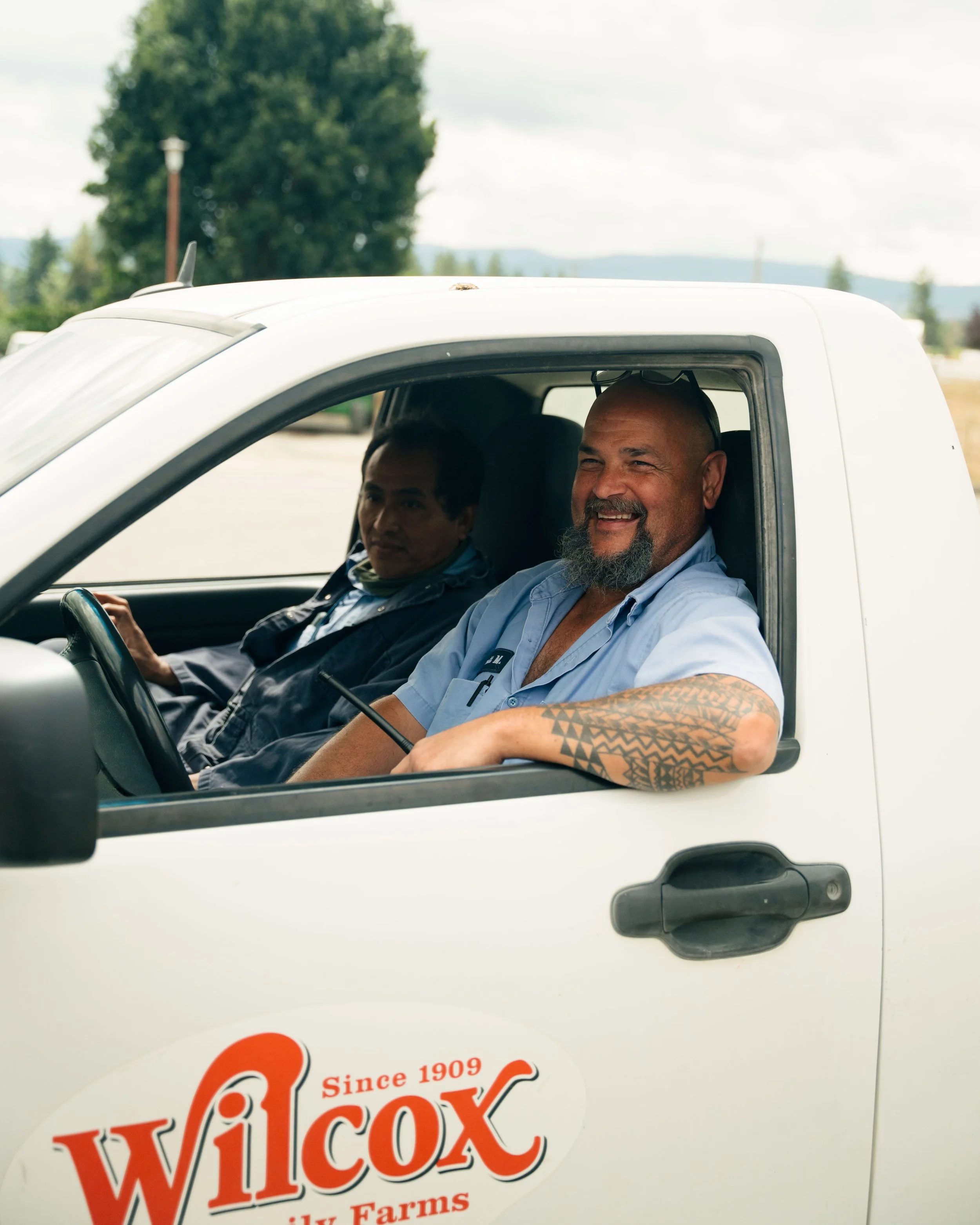 Two Wilcox Farms team members in uniform seated in a Wilcox truck, representing the people behind the farm’s daily operations.