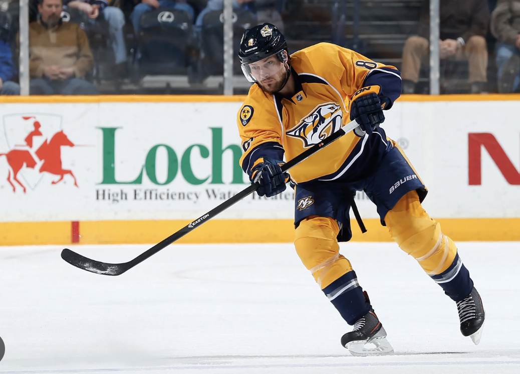An ice hockey player wearing a yellow and navy jersey with a tiger logo, number 8, and a black helmet, skating on the ice during a game.