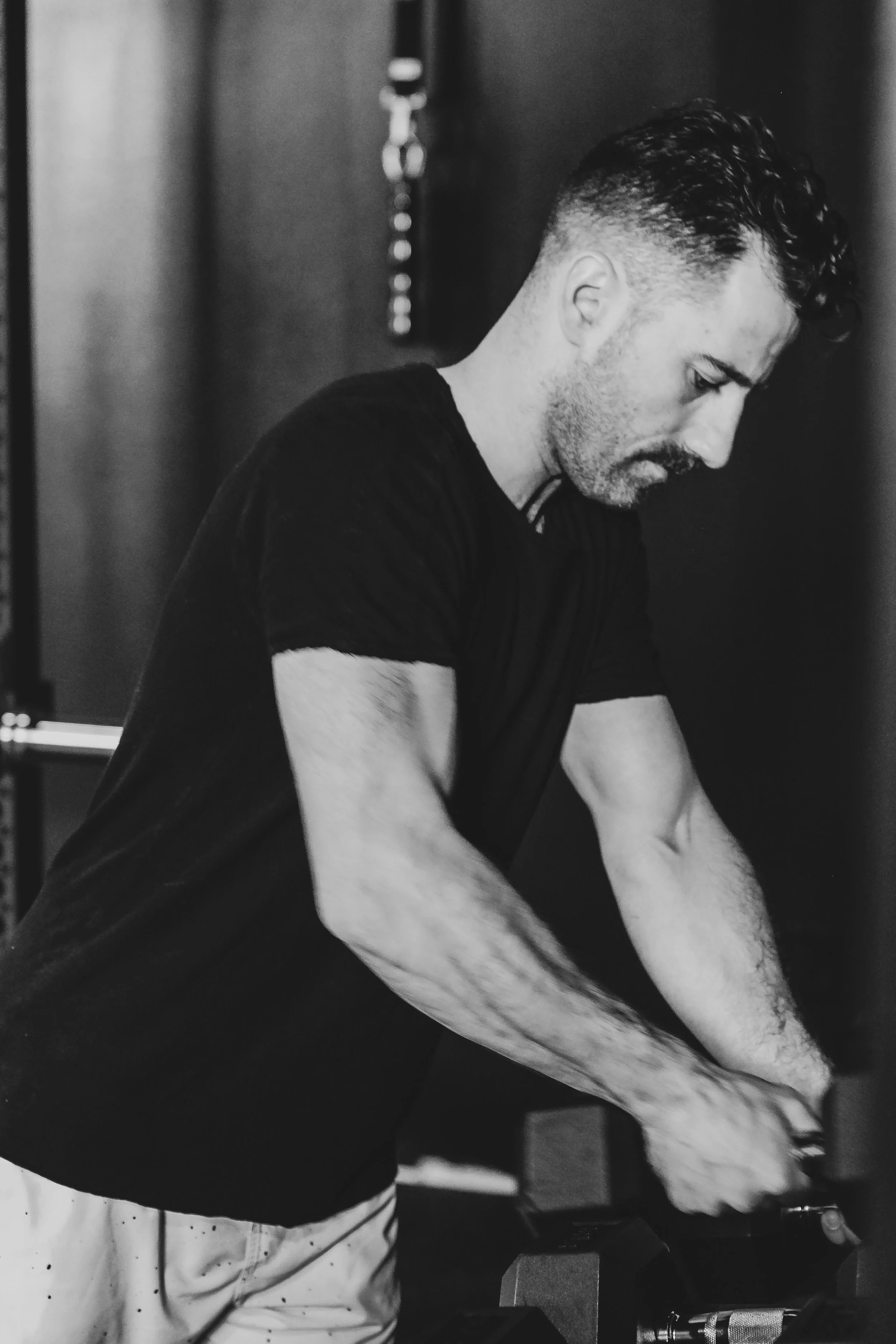 A man with short hair and tattoos on his arms, wearing a black t-shirt, appears to be focused on assembling or fixing something with his hands.