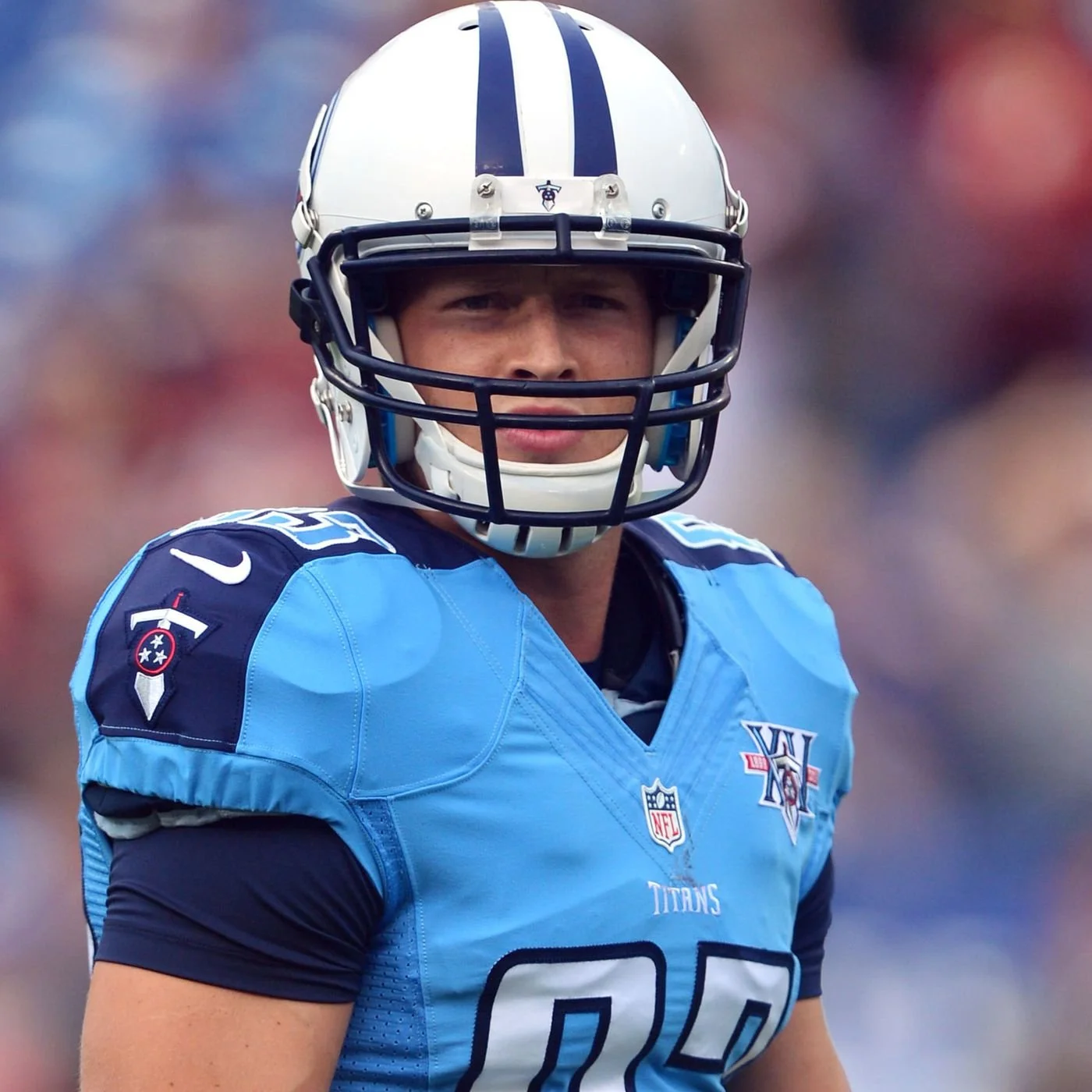 A football player wearing a light blue Tennessee Titans uniform and helmet, looking towards the camera with a serious expression, on the field.