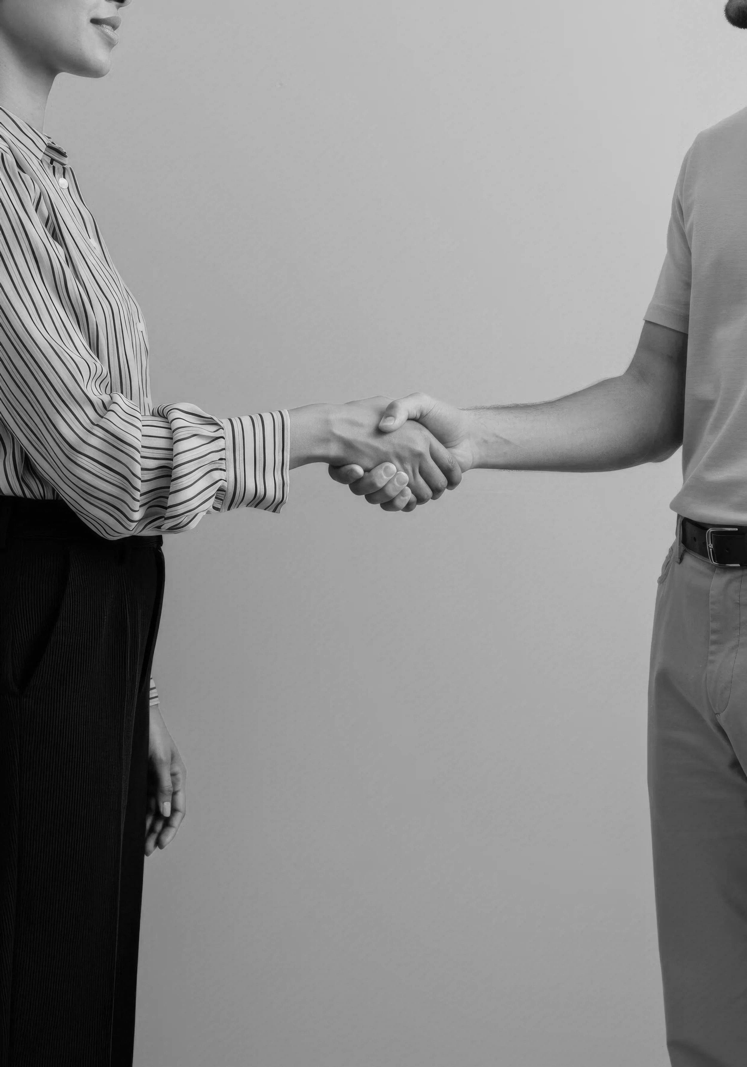 Two people shaking hands, one wearing a striped shirt and the other wearing a plain t-shirt, against a plain background.