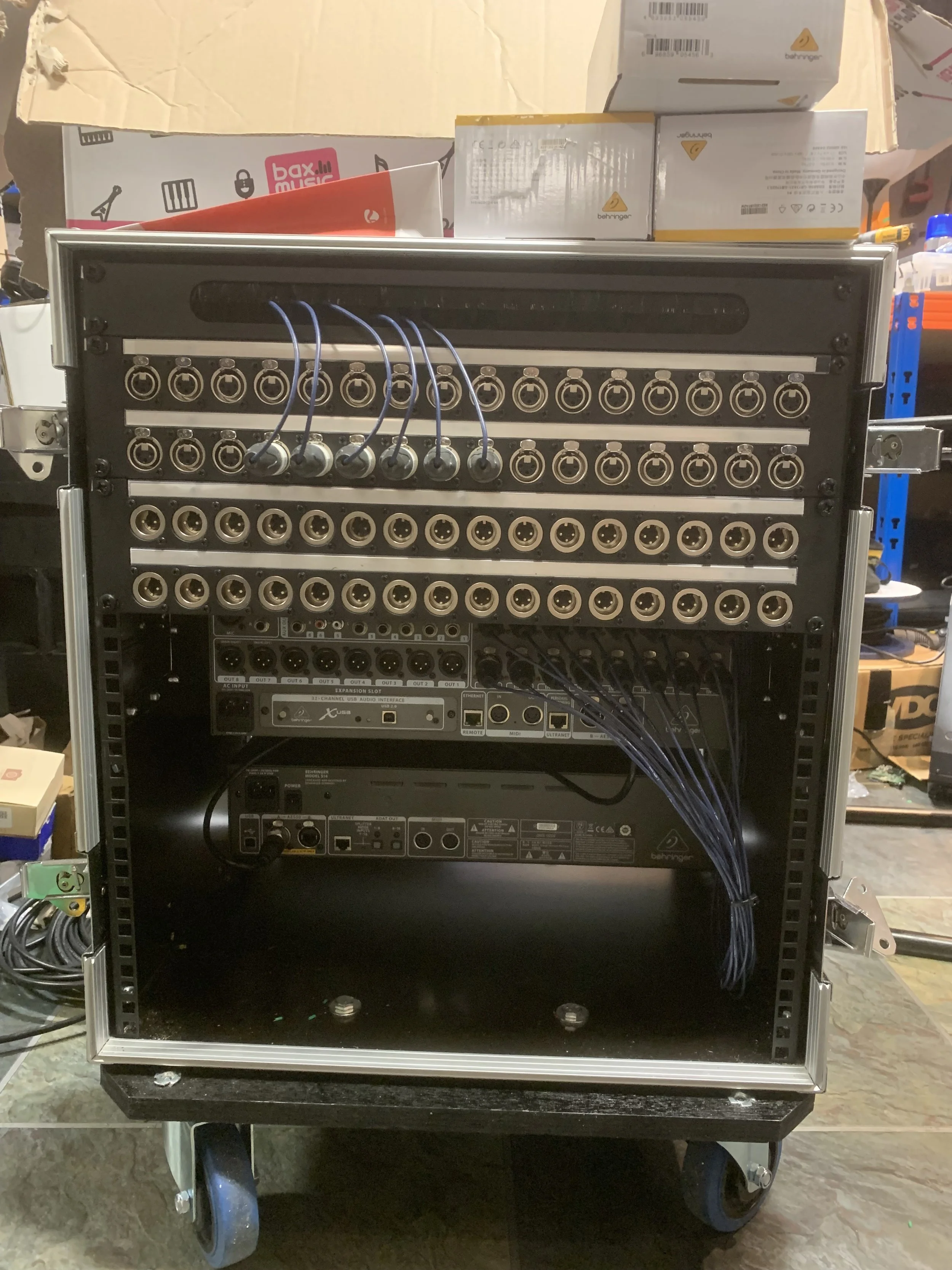 Rear view of an in ear monitor rack with multiple input and output ports, connected by numerous cables, in a workshop or storage area.