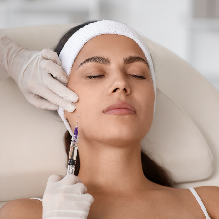 Young woman receiving a facial injection or cosmetic treatment about her cheek area in a medical spa or clinic setting.