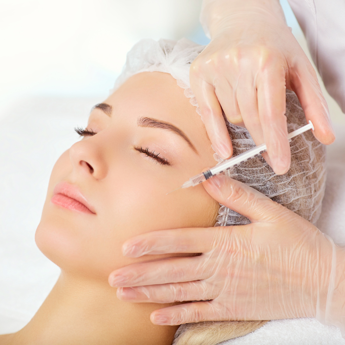 A woman receives a cosmetic injection in her face from a healthcare professional wearing gloves.