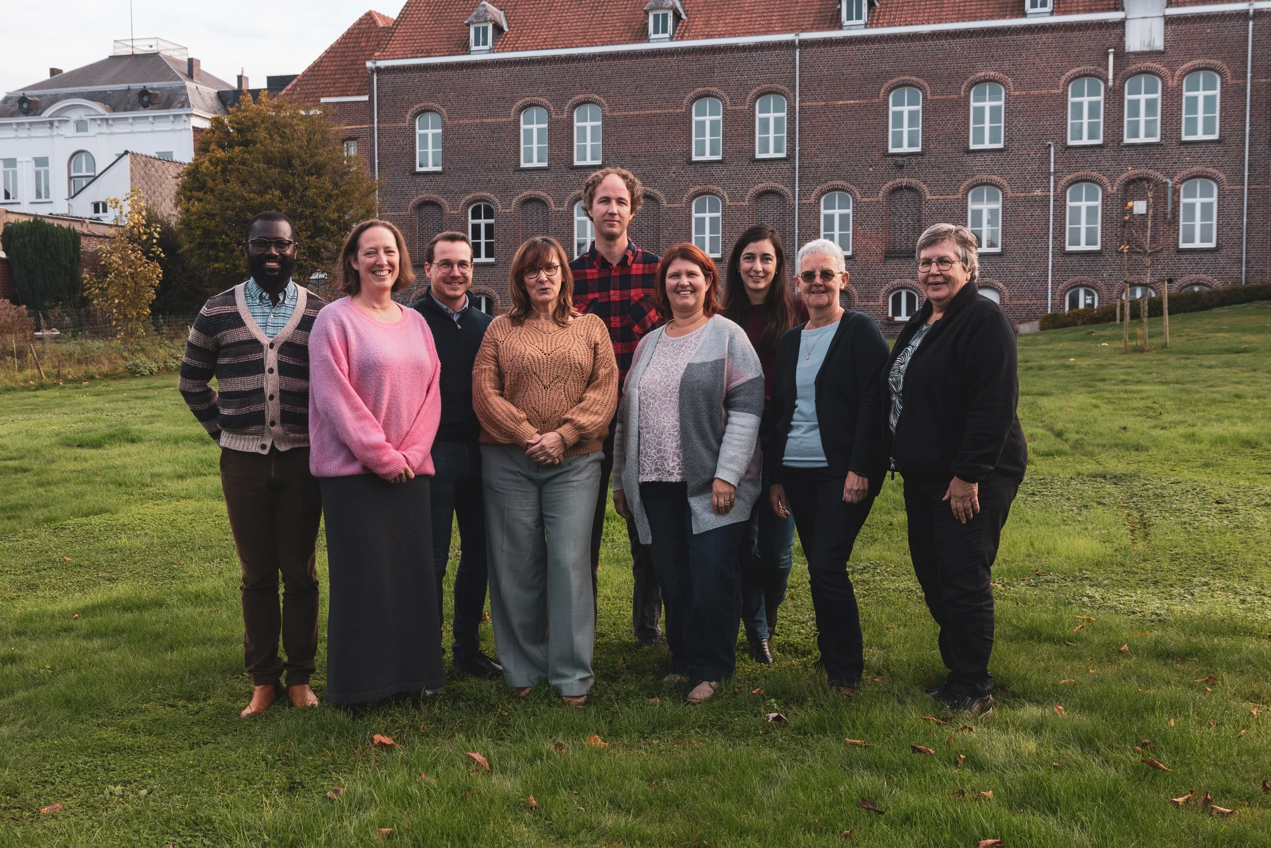 Modern wooden and metal building with large glass window, set against a mountain landscape, surrounded by low bushes and grass.
